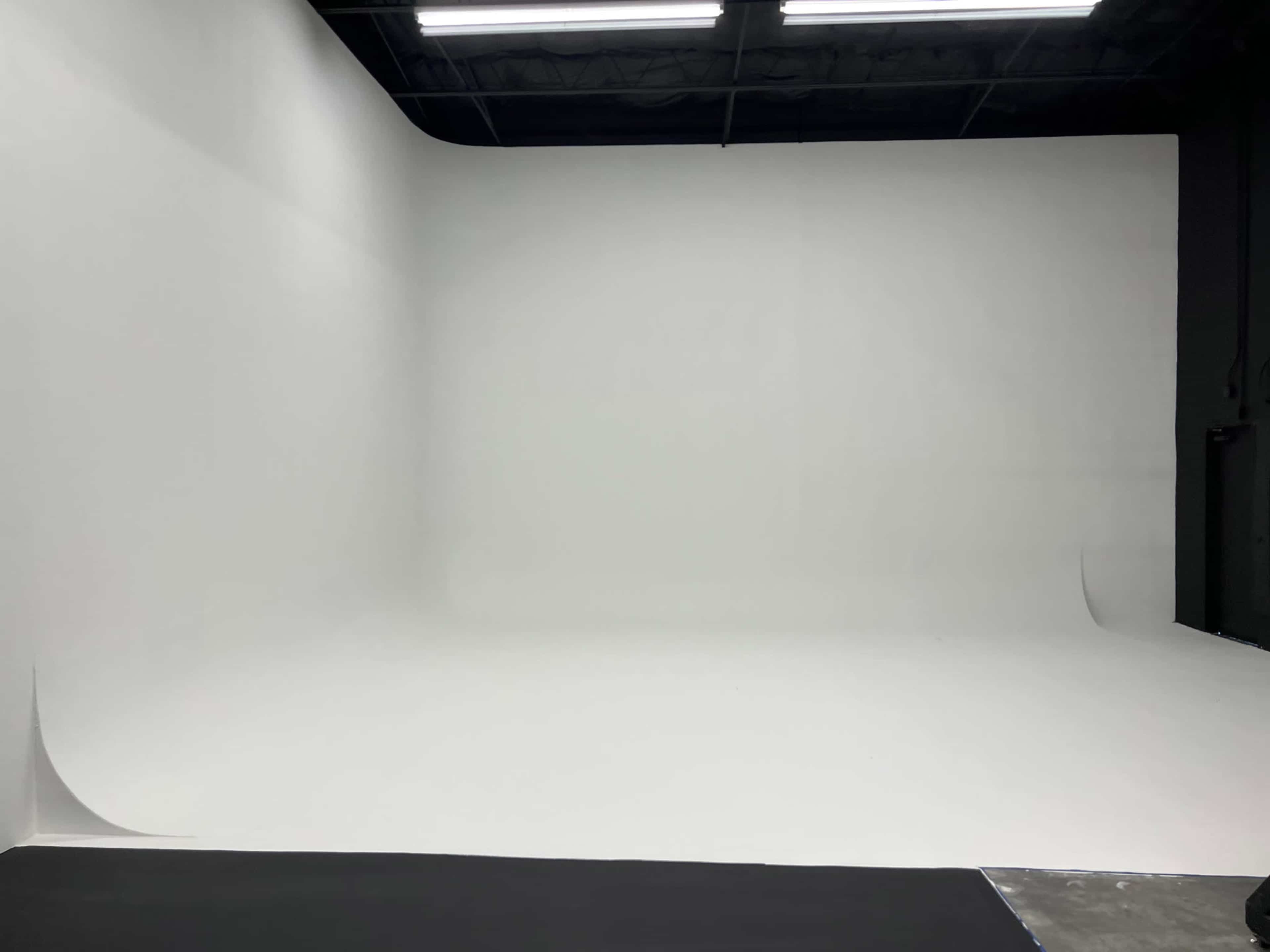 An empty photo studio with a seamless white backdrop and a dark floor.