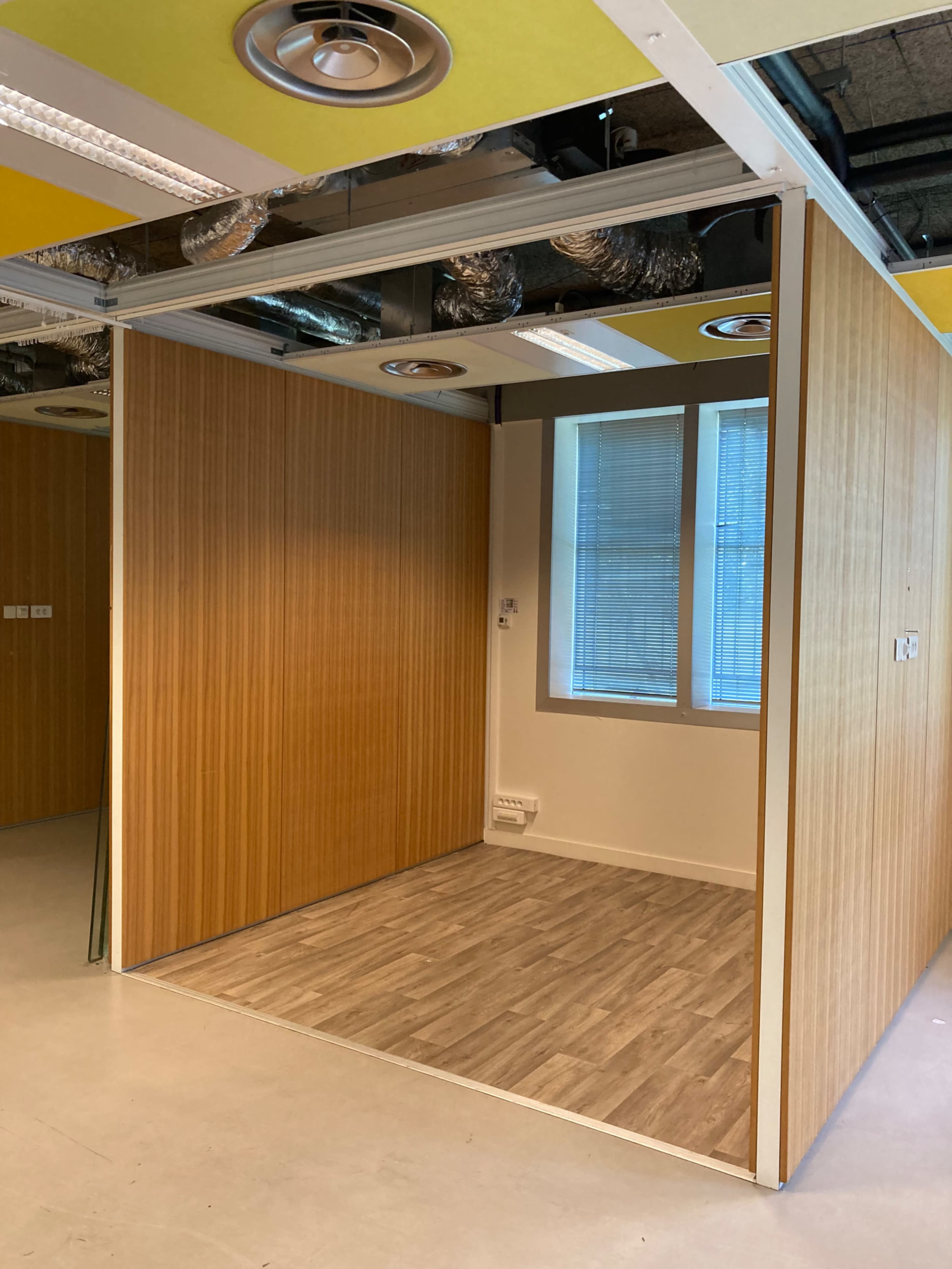 The image shows a partially enclosed office space with wooden panel walls and a window letting in natural light.