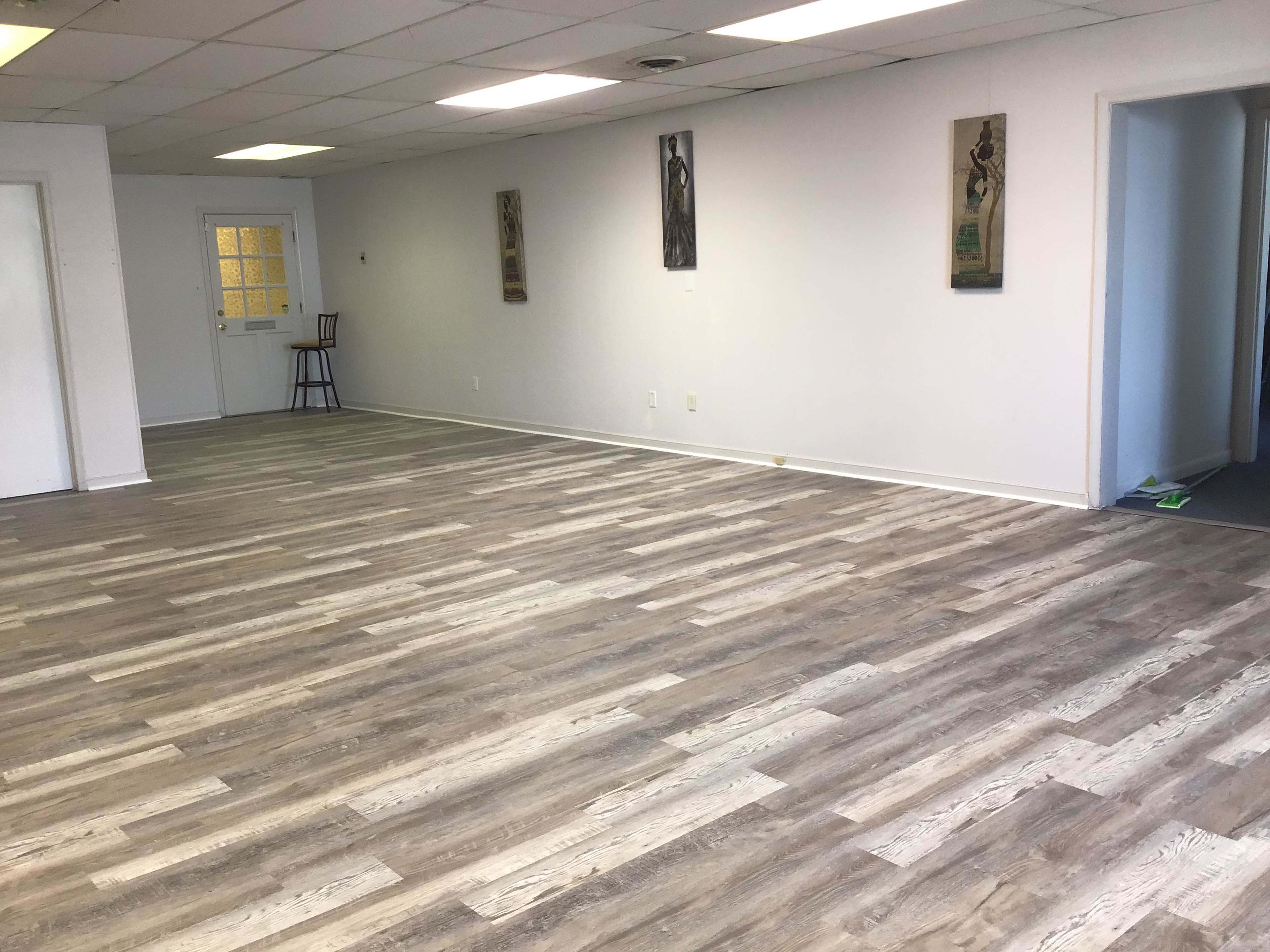 A spacious, empty room with light-colored wooden flooring and two pieces of wall art hung on the left wall.
