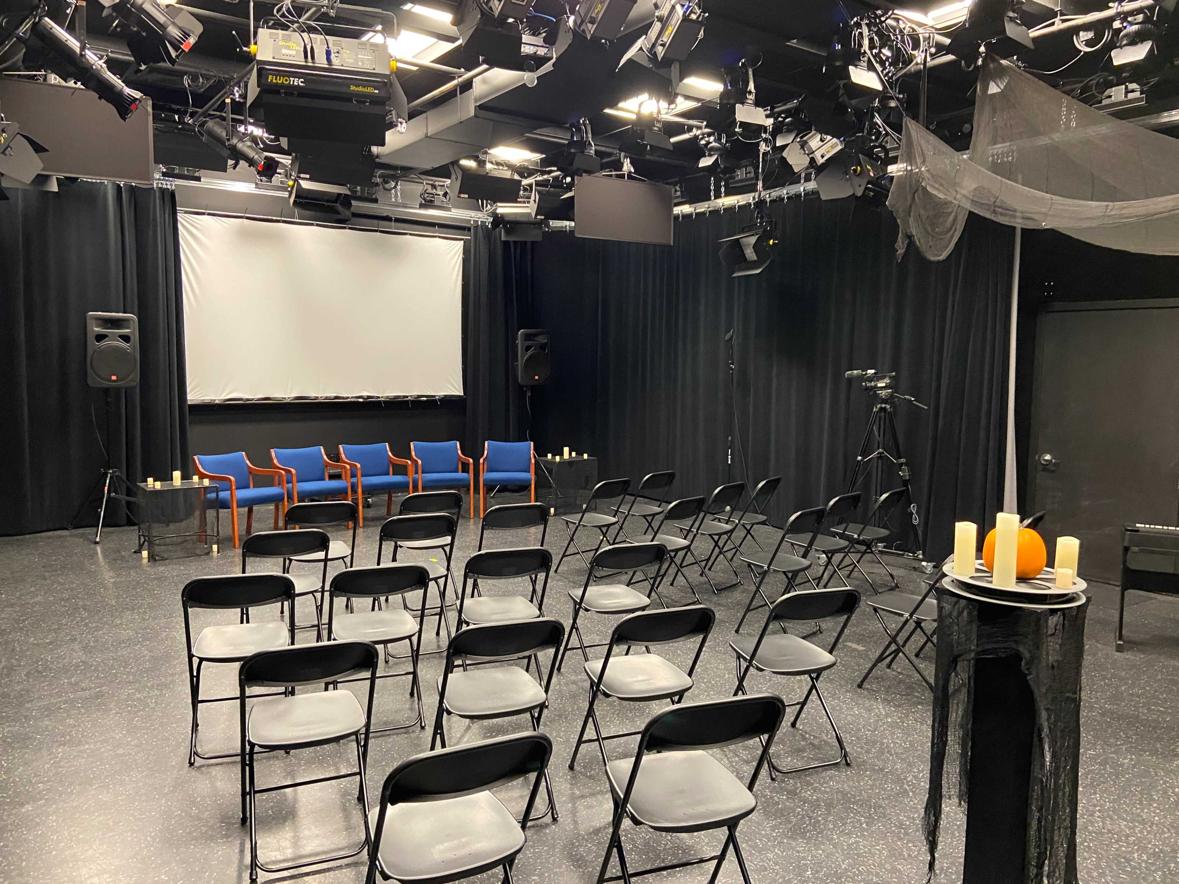 A small theater set up with black chairs facing a screen, flanked by three blue chairs and adorned with candles on a table.