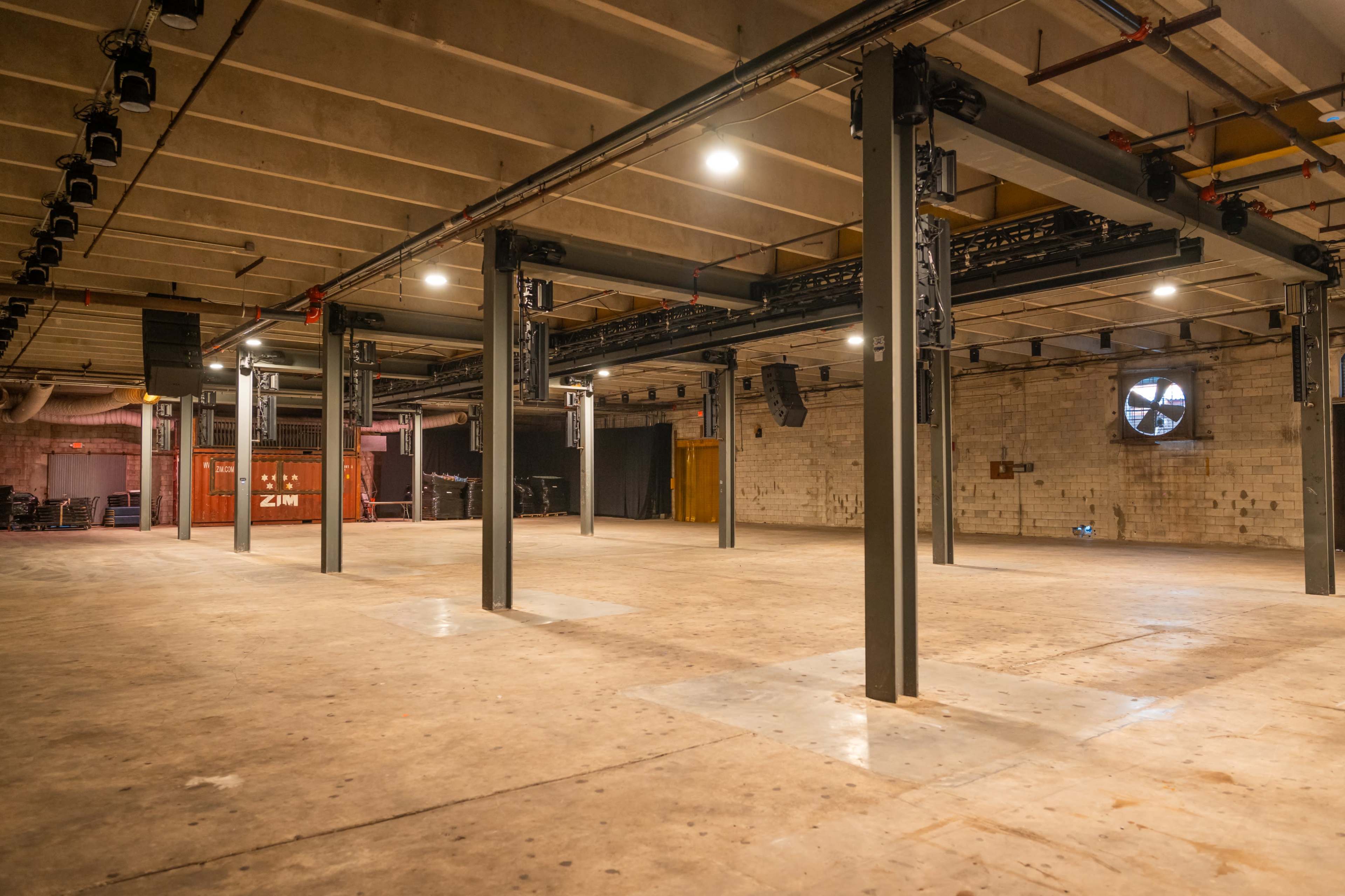 The image shows an empty industrial space with exposed beams and metal structures, illuminated by overhead lights.