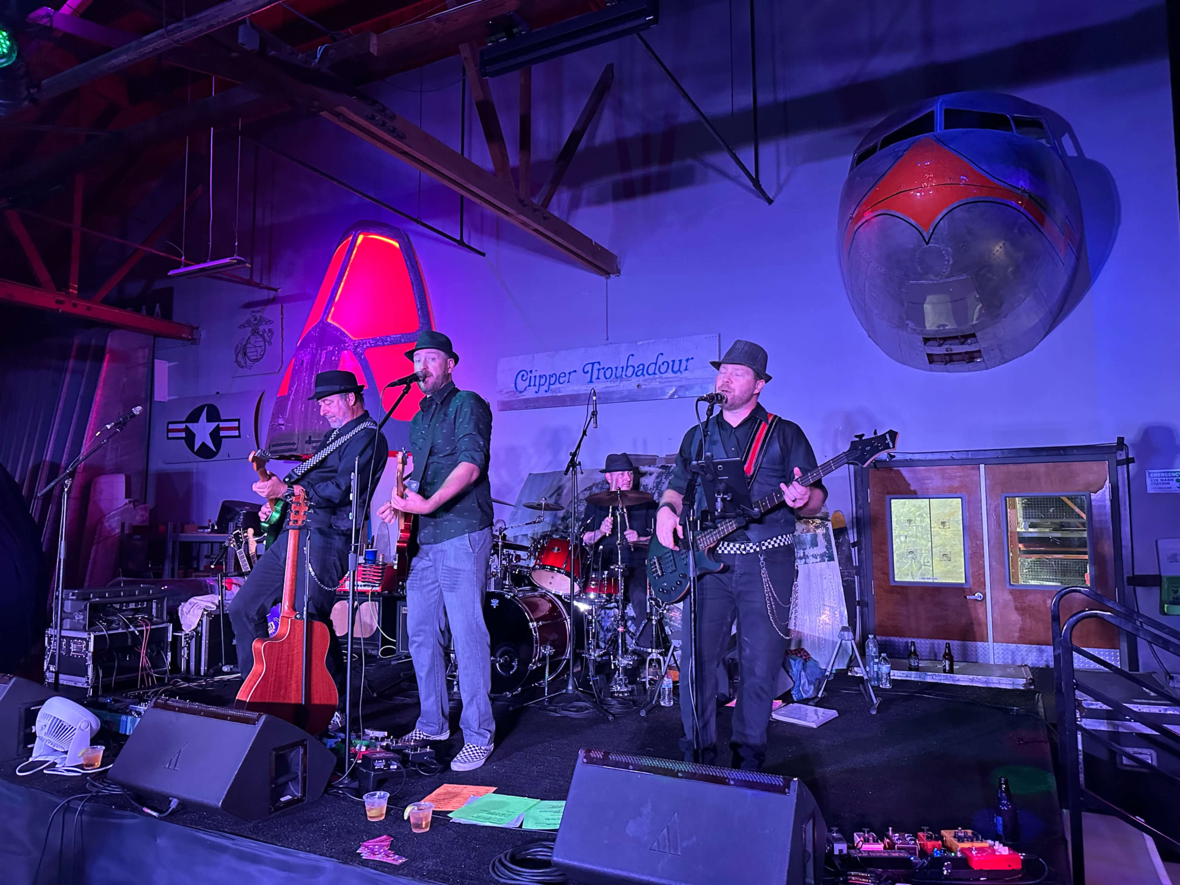A band performs on stage in a venue featuring an airplane fuselage in the background.