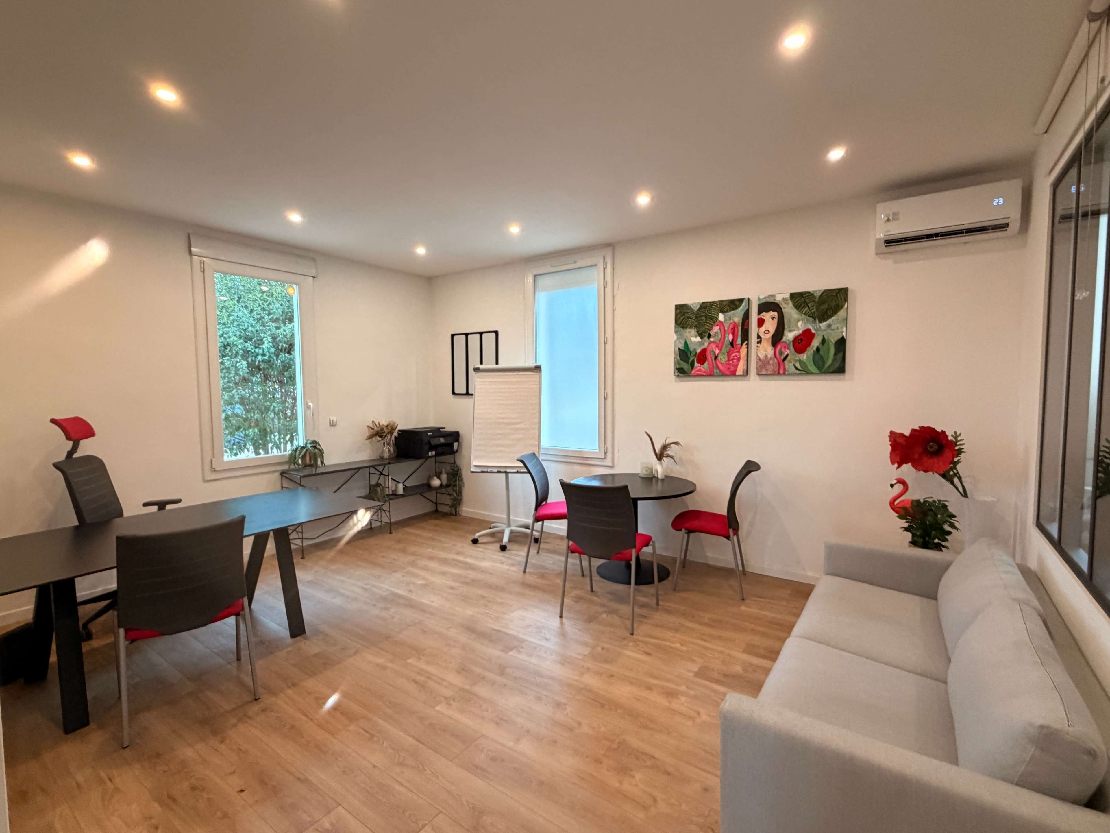 The image shows a modern office space with a large table, several chairs, a sofa, and a whiteboard, illuminated by recessed lighting.