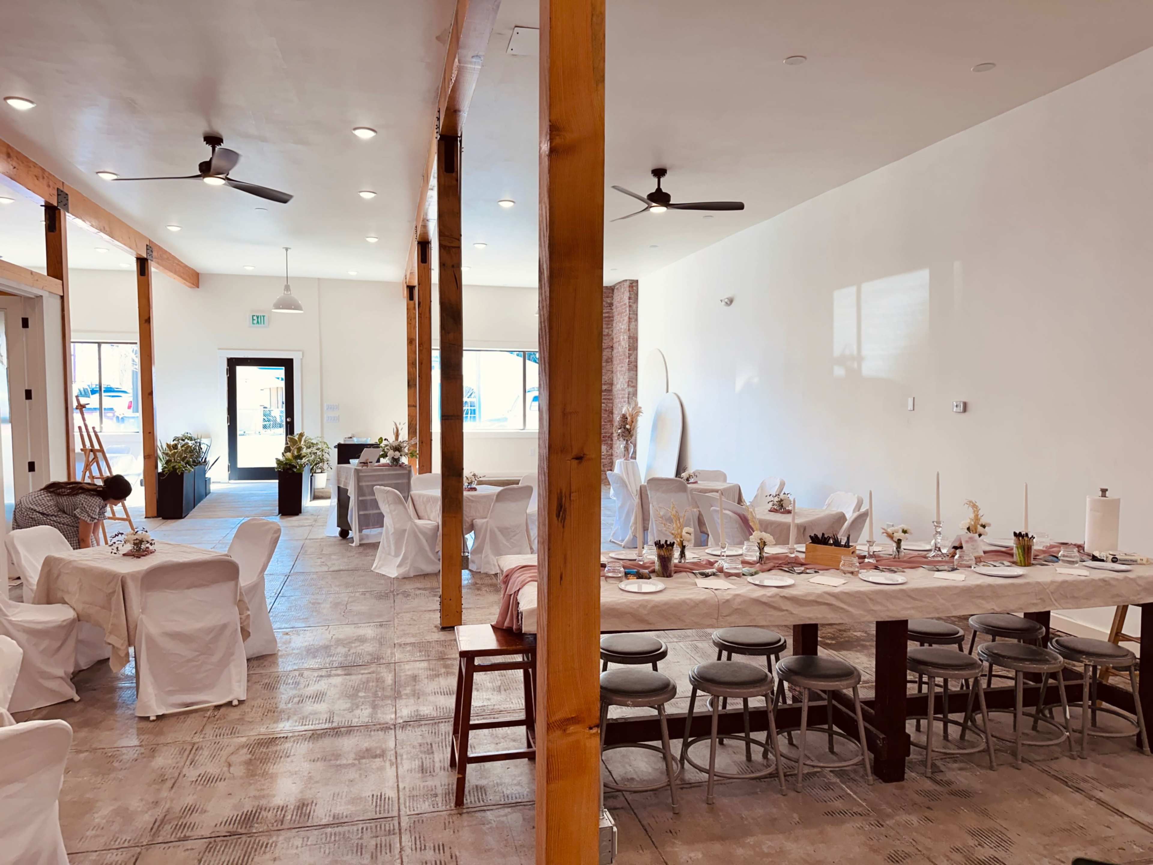 A spacious dining area with wooden beams, several tables set for a meal, and a minimalist decor style.