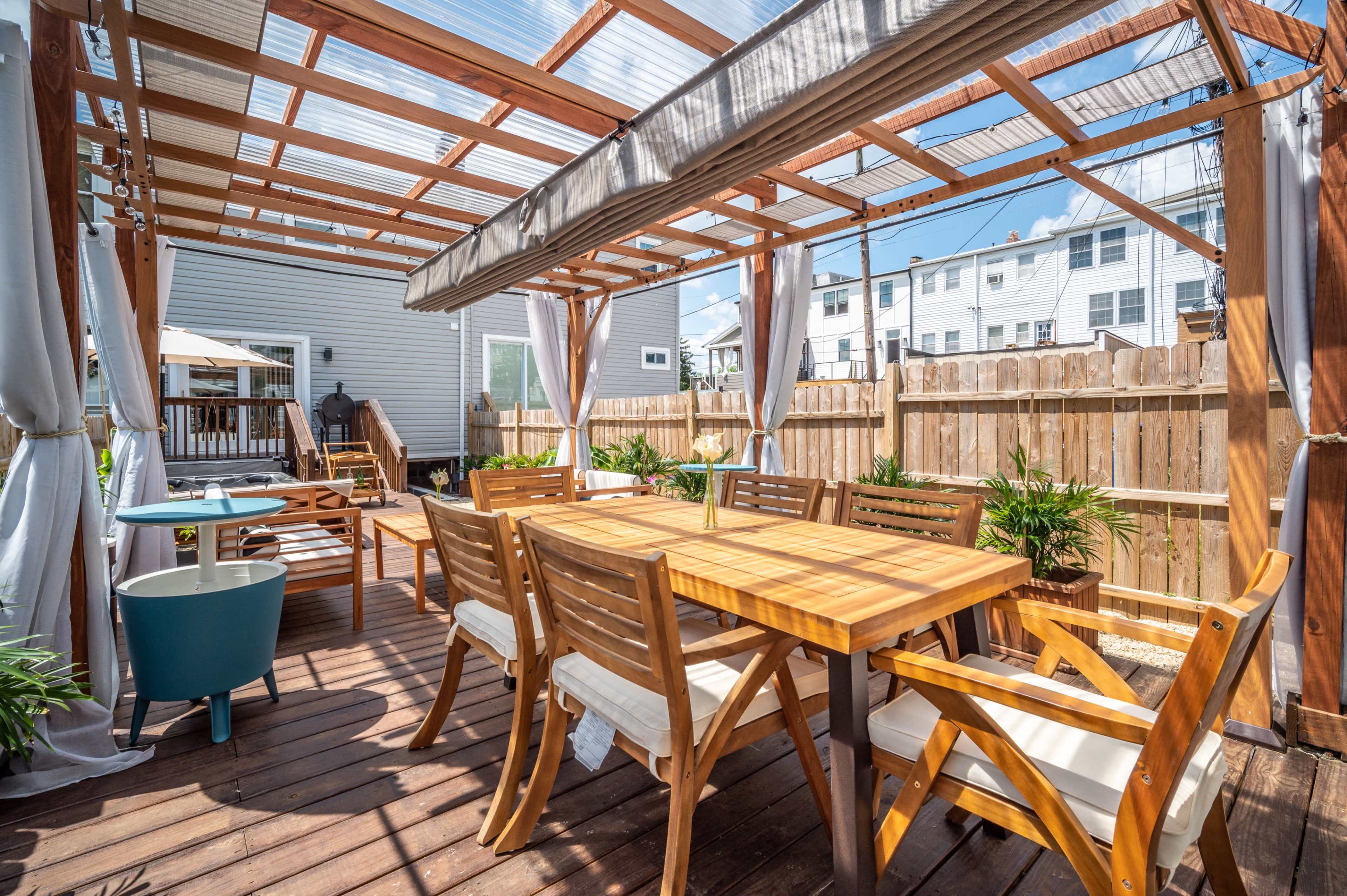 A wooden patio with a dining table and chairs, surrounded by plants and a pergola.