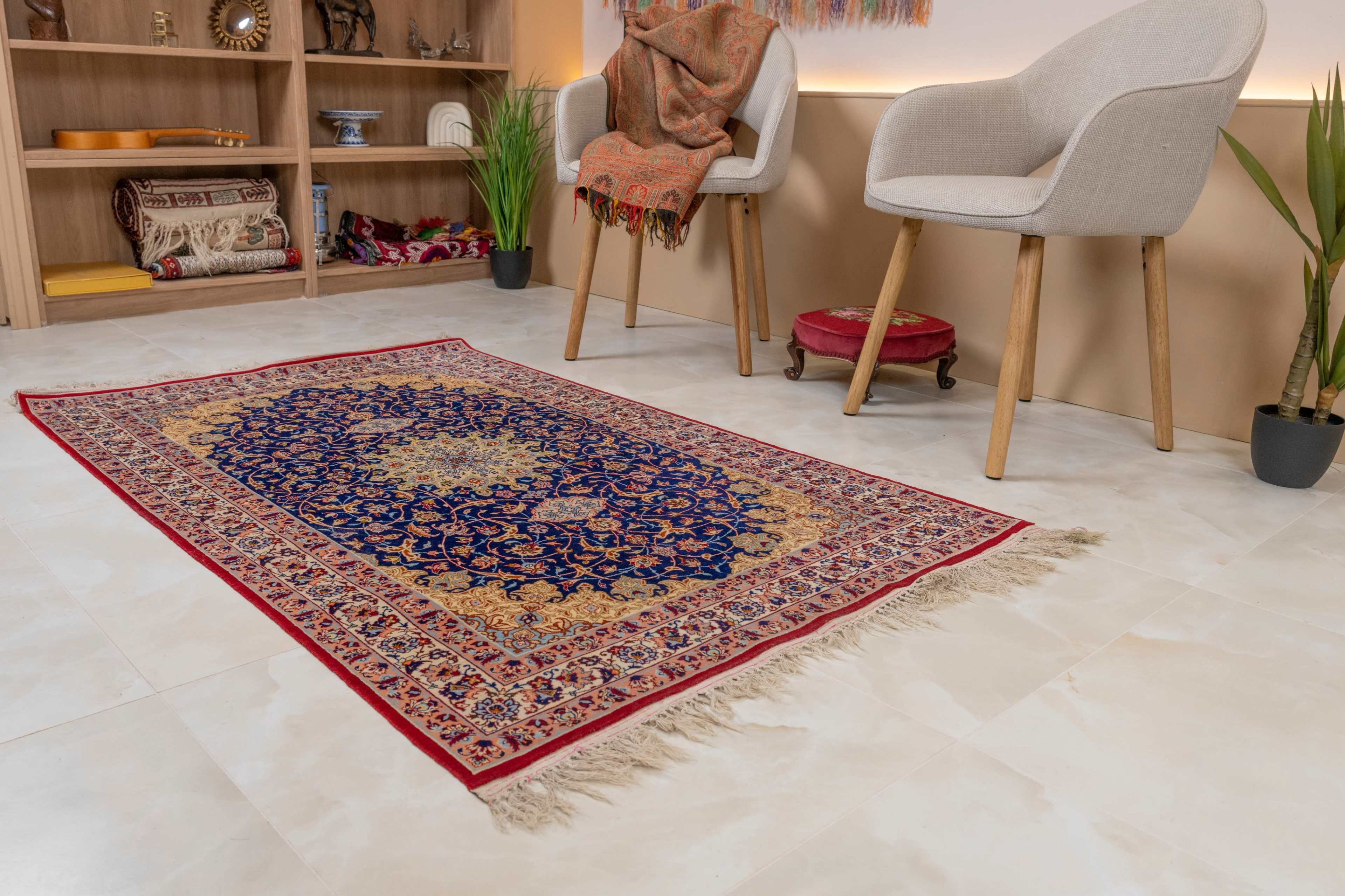 A decorative area rug with an intricate blue and gold pattern lies on a tiled floor, surrounded by two modern chairs and a potted plant.