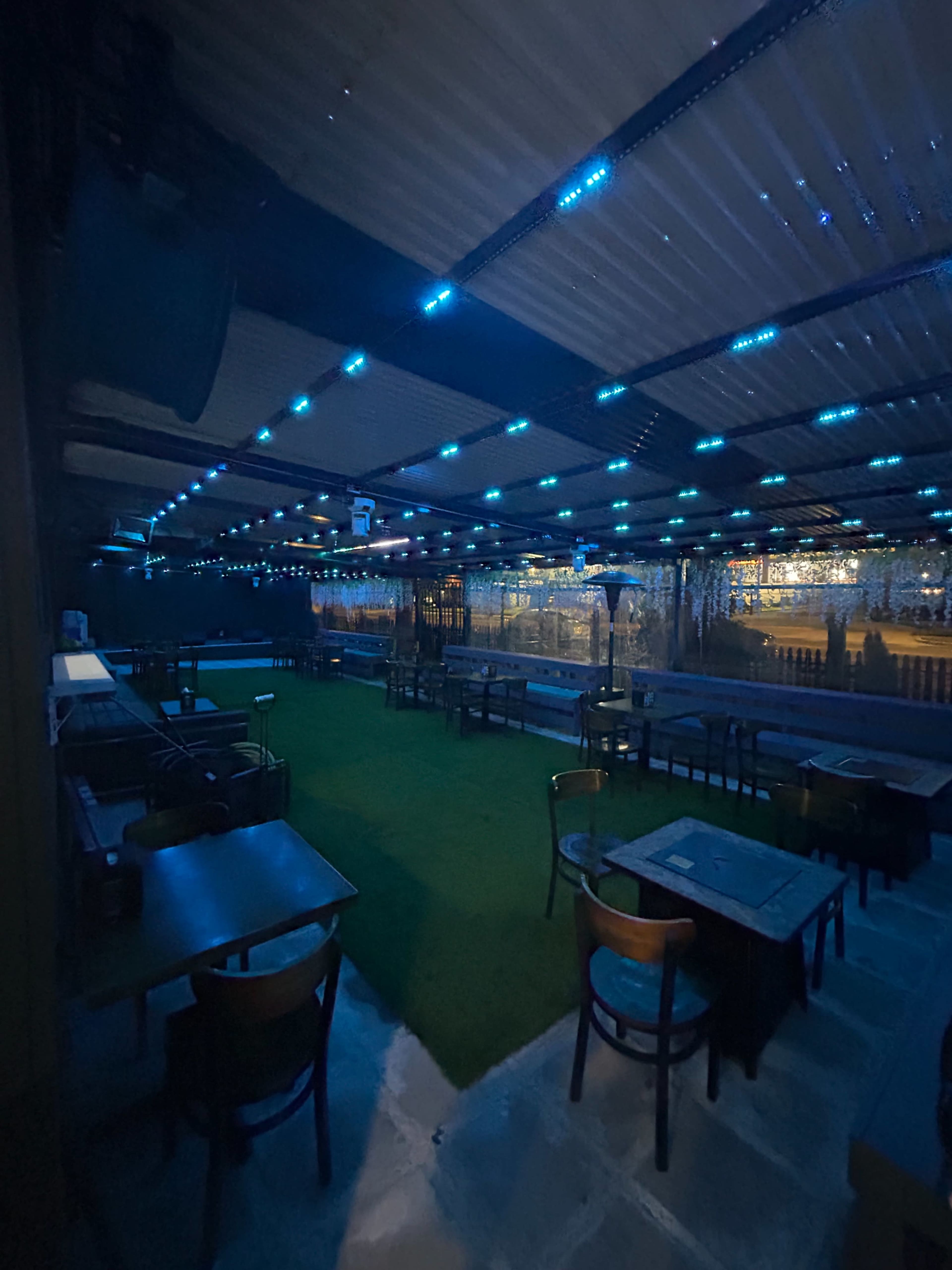 The image shows an empty outdoor seating area of a restaurant or bar, illuminated by blue LED lights.