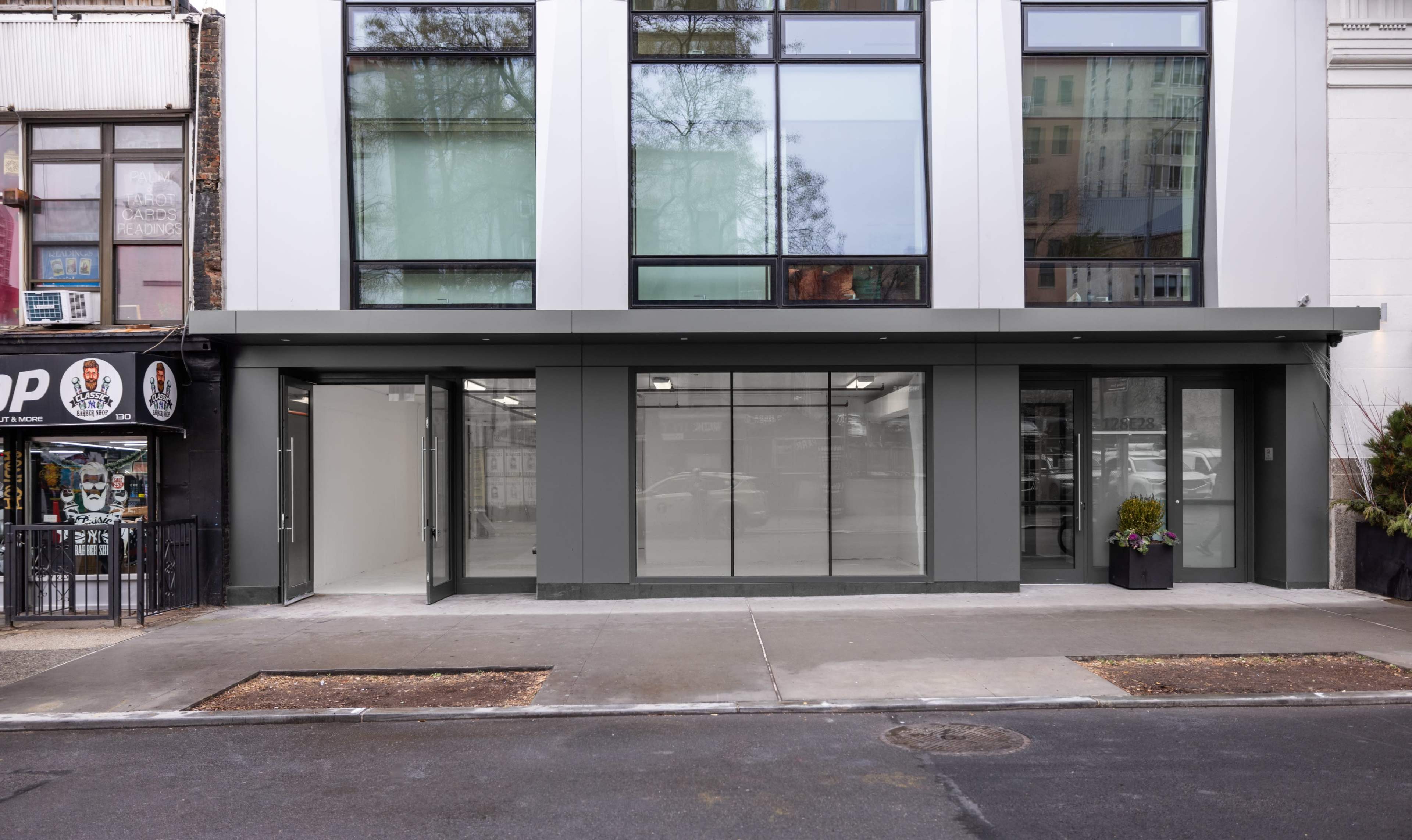 A modern commercial building with a large glass storefront and an empty adjacent space, situated on a city street.