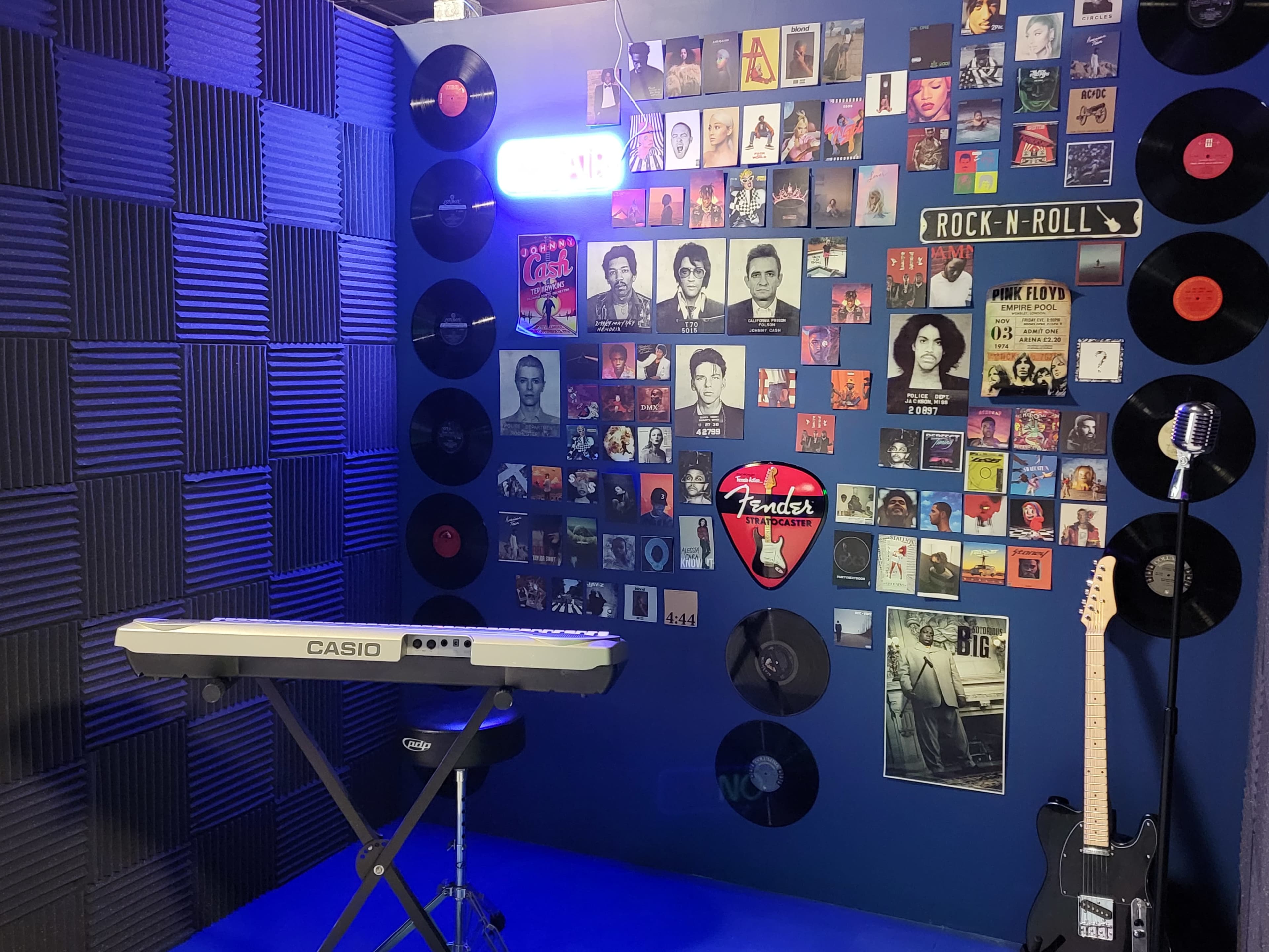 The image features a music-themed room with a keyboard on a stand, a microphone, and walls adorned with framed album covers and vinyl records.