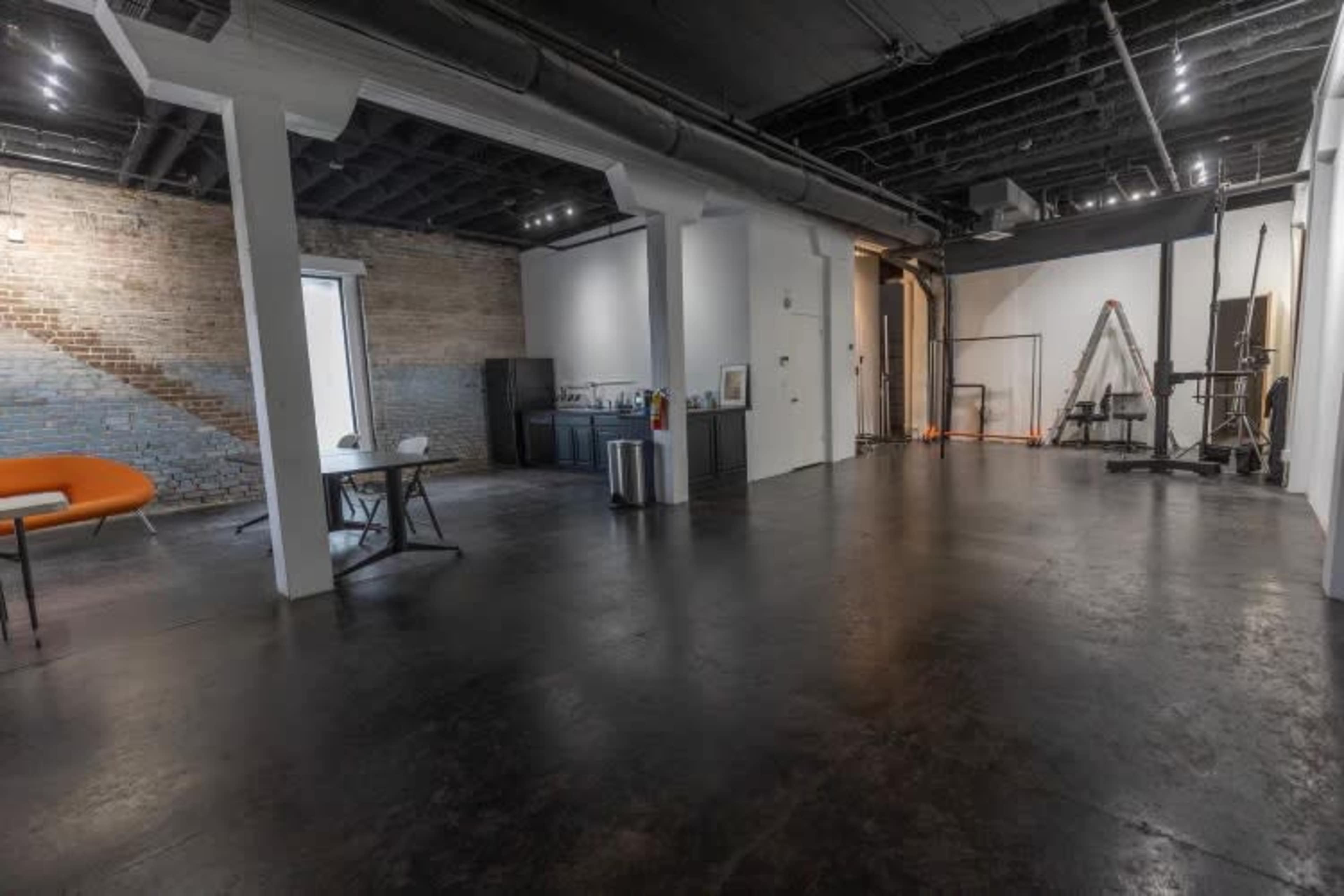 A spacious industrial-style room with a polished concrete floor, exposed brick walls, and various furniture pieces, including an orange sofa and a table.