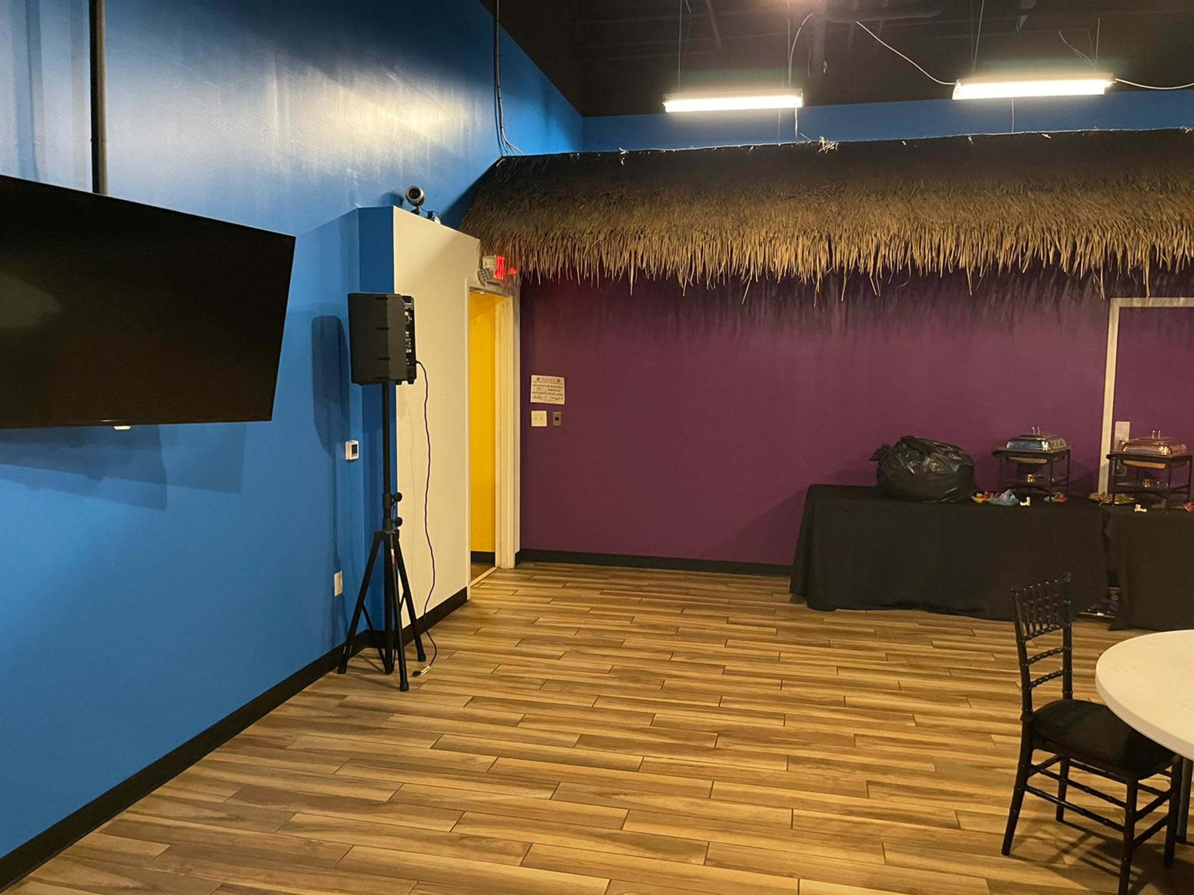 A brightly colored room with a blue wall, purple accents, a thatched roof area, and a set-up for catering on a table.