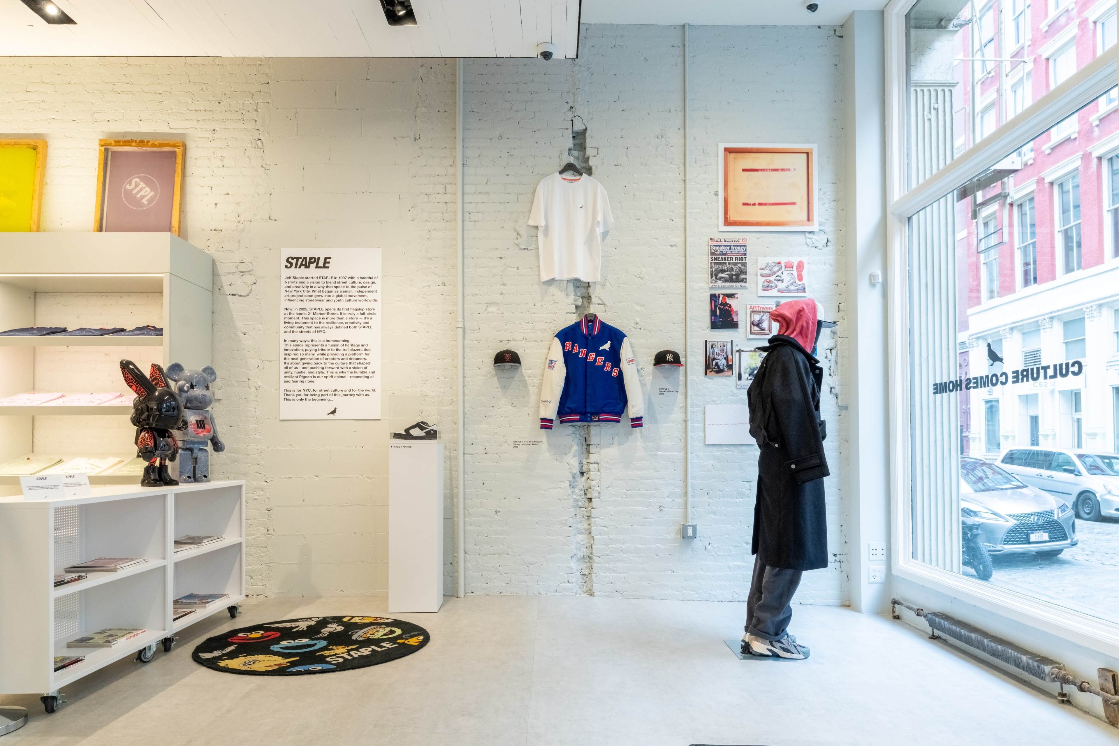 The image shows a retail space with a person wearing a coat and a headscarf, standing in front of clothing and merchandise displayed on a wall and shelves.