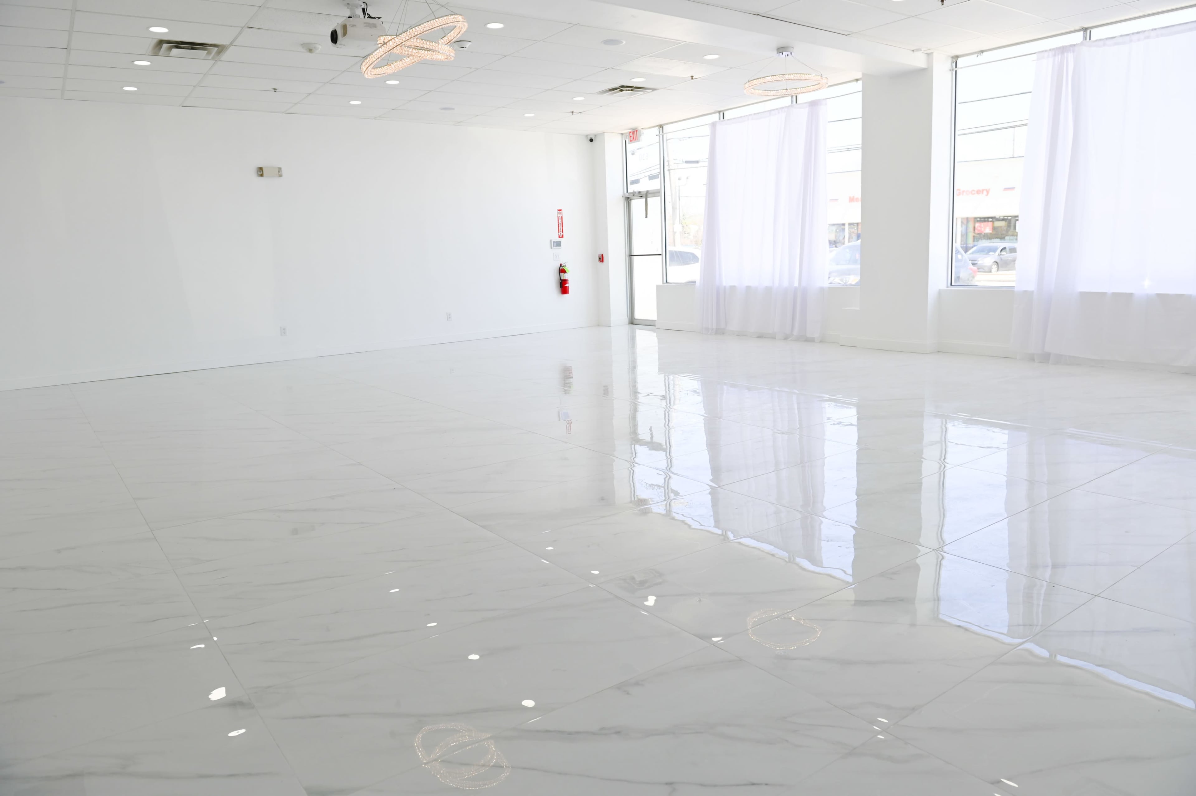 A spacious room with white walls, large windows, and shiny marble flooring.