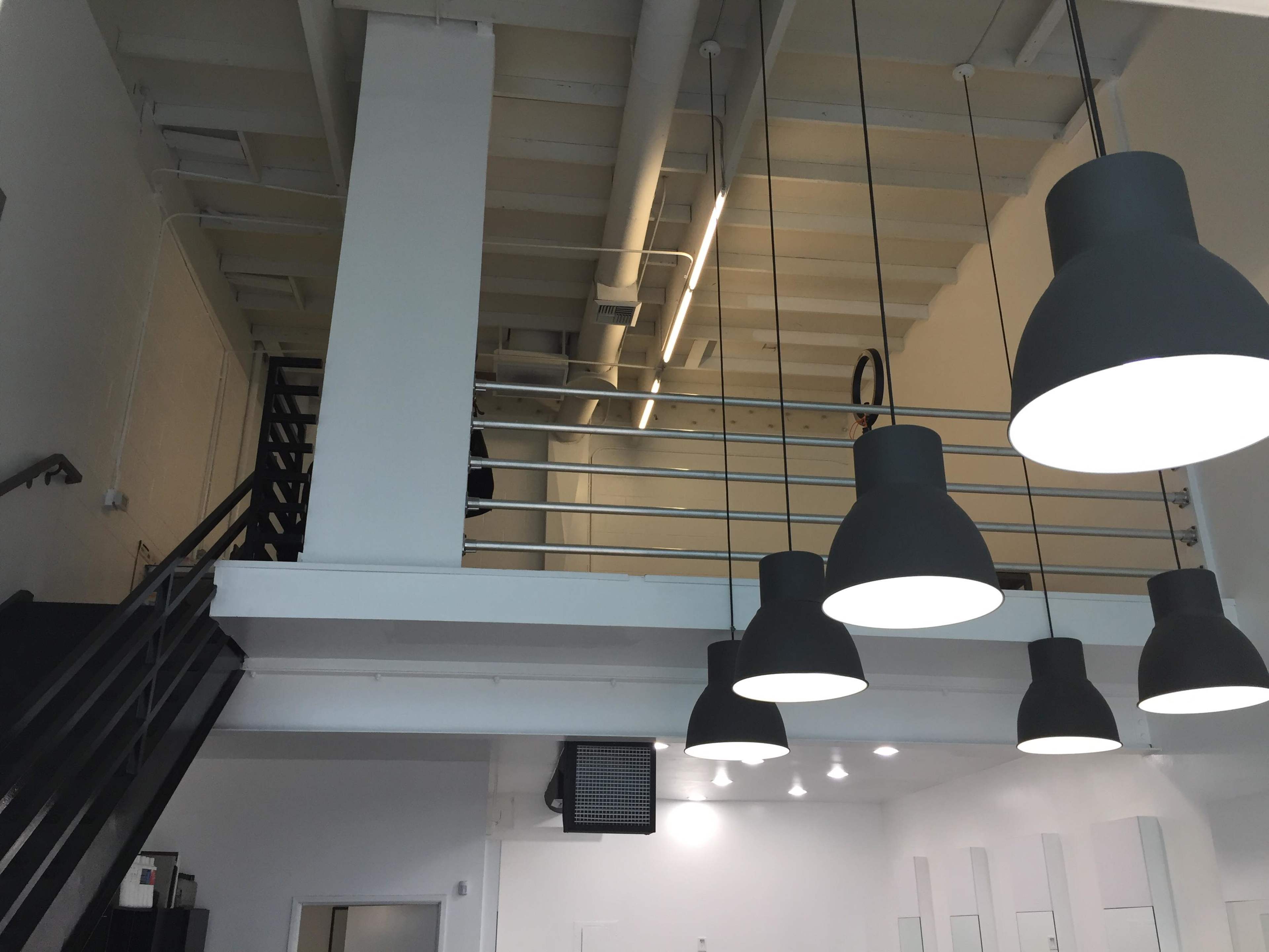 A modern interior with a staircase leading to a second level, featuring large hanging light fixtures and a minimalistic design.
