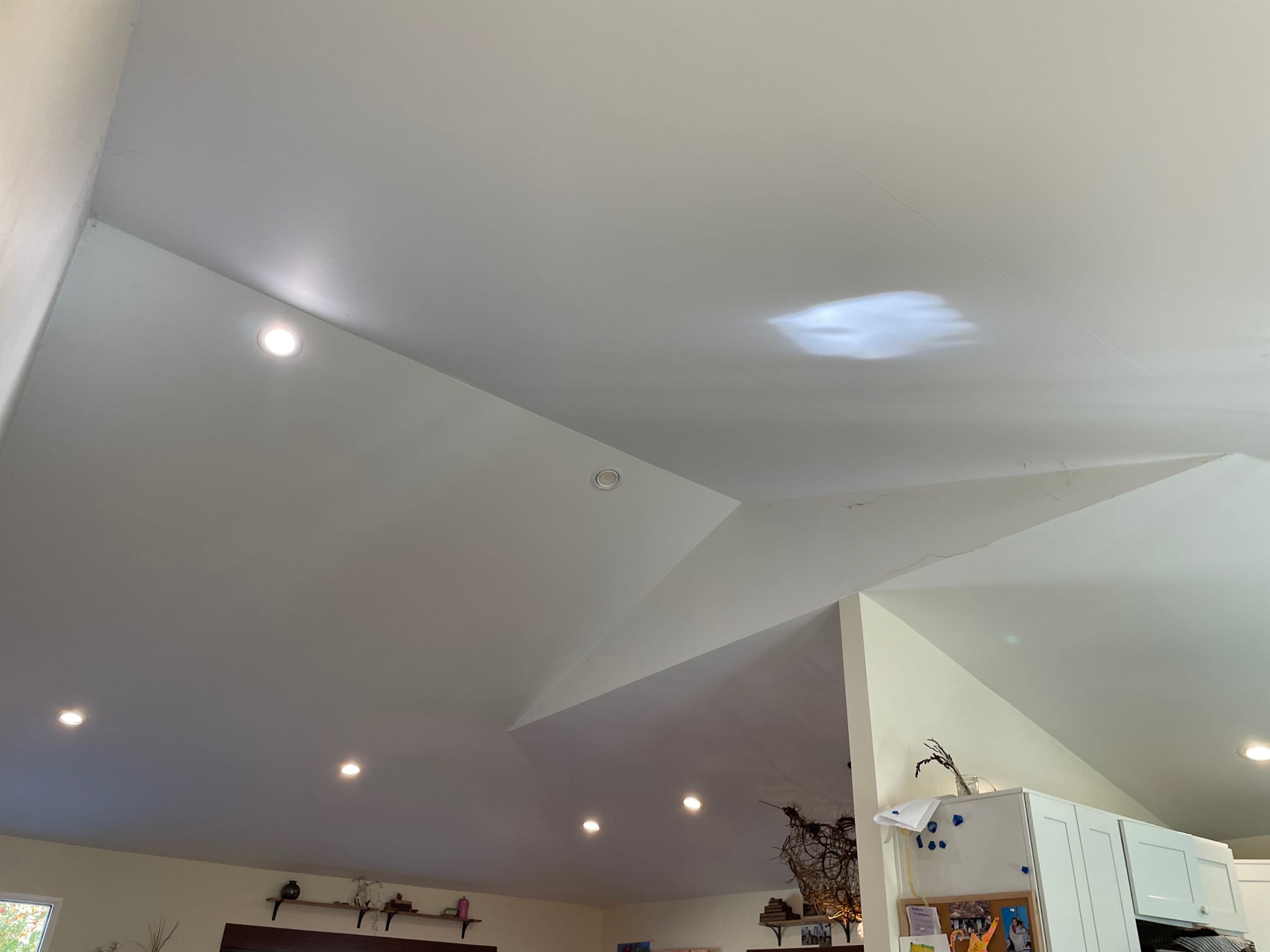 A room with a ceiling that has varying elevations and recessed lighting, along with a light reflection on one section.