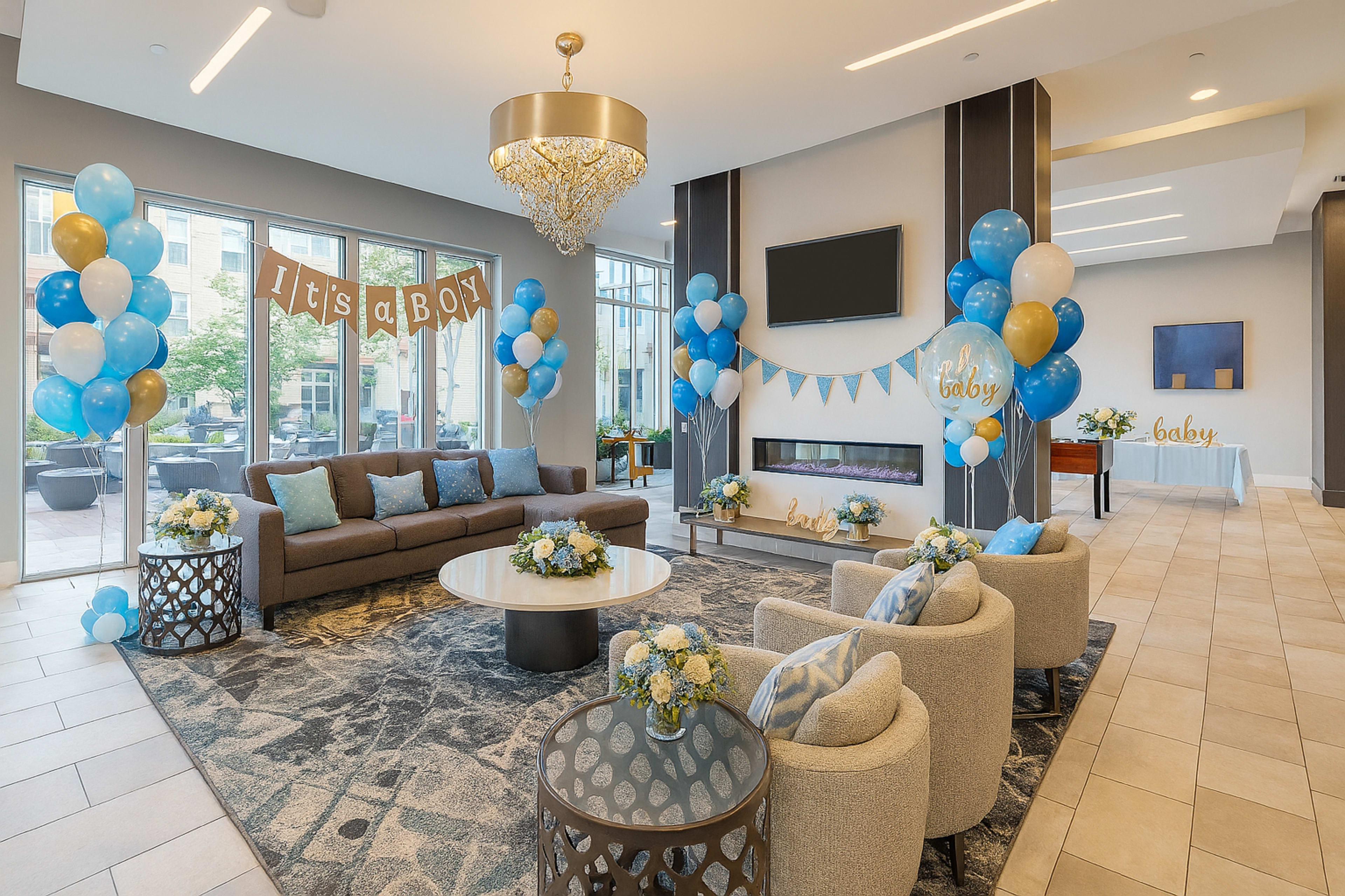 A modern lounge area is decorated with blue and gold balloons and banners for a baby shower celebration.