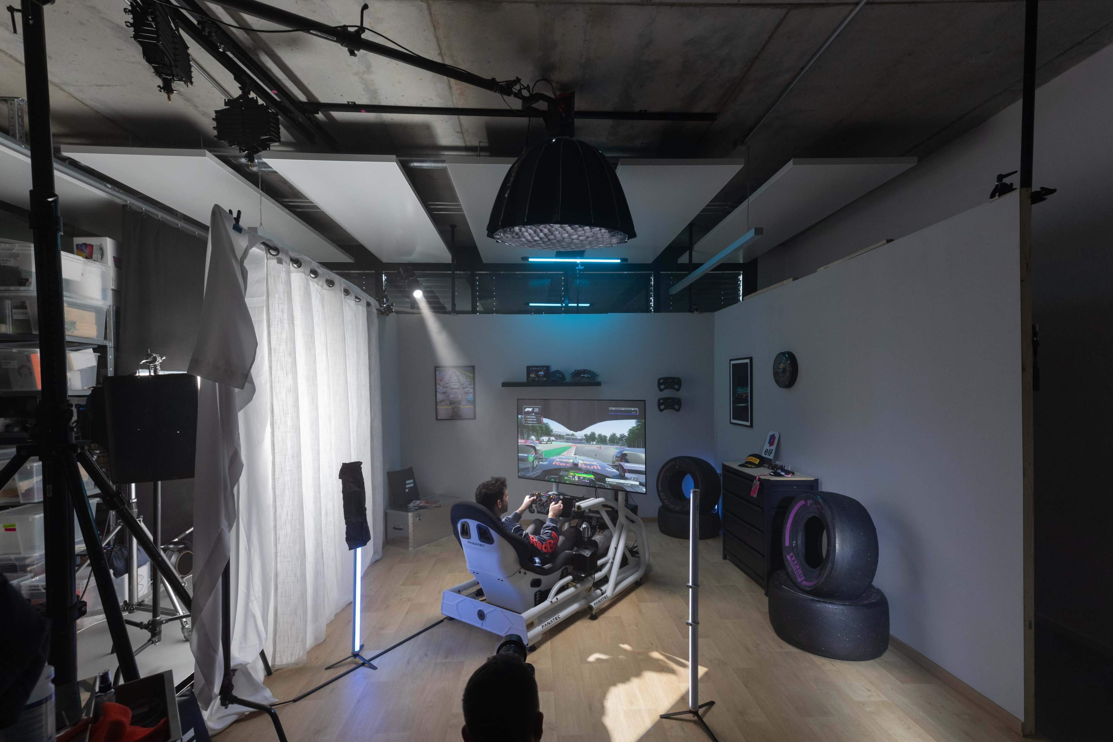A person sits in a racing simulator in a well-lit room, focused on a gaming screen displaying a racing game.