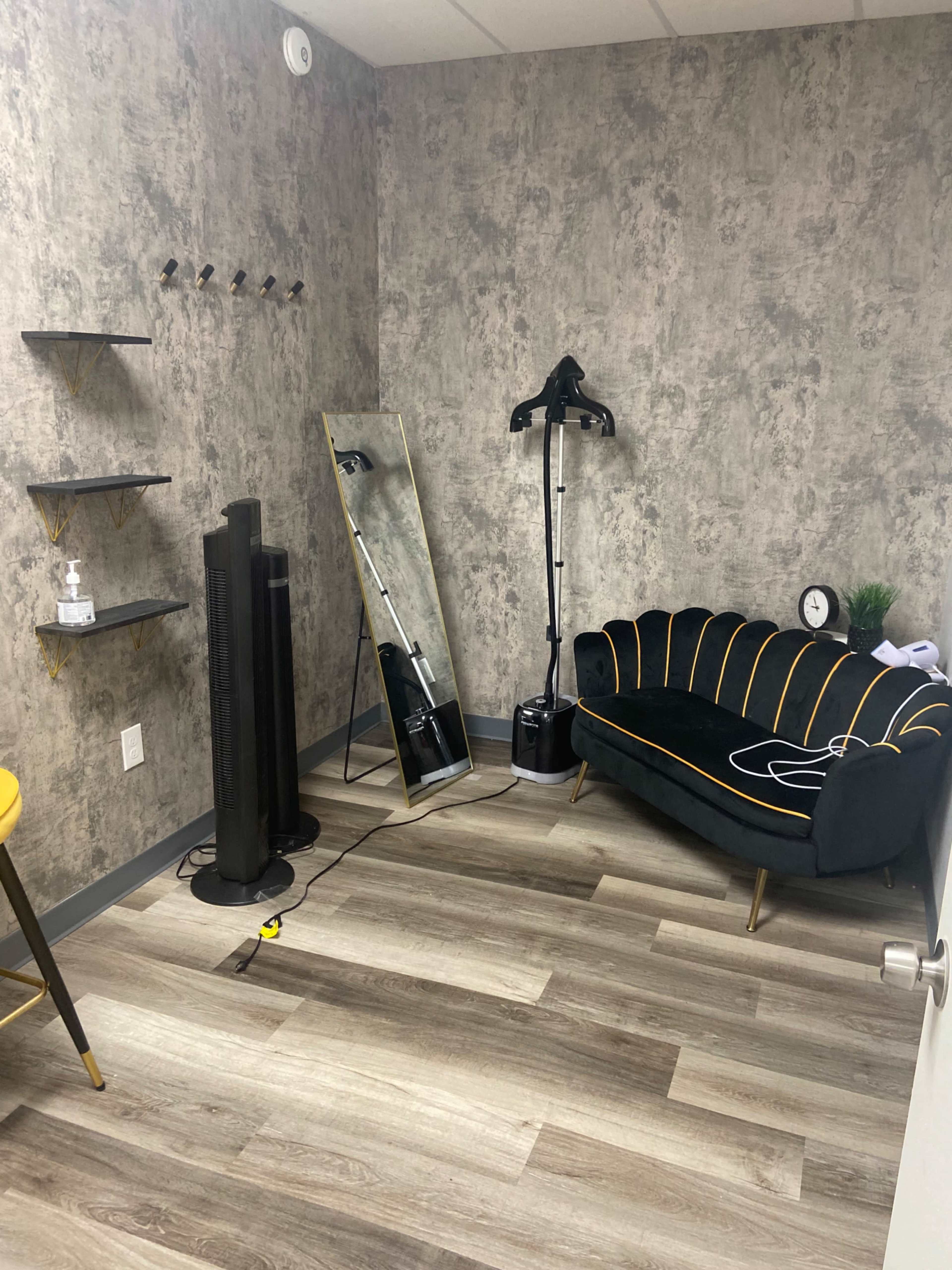 A modern room with a patterned wall, a black and yellow couch, a large mirror, a standing lamp, and shelves on one side.
