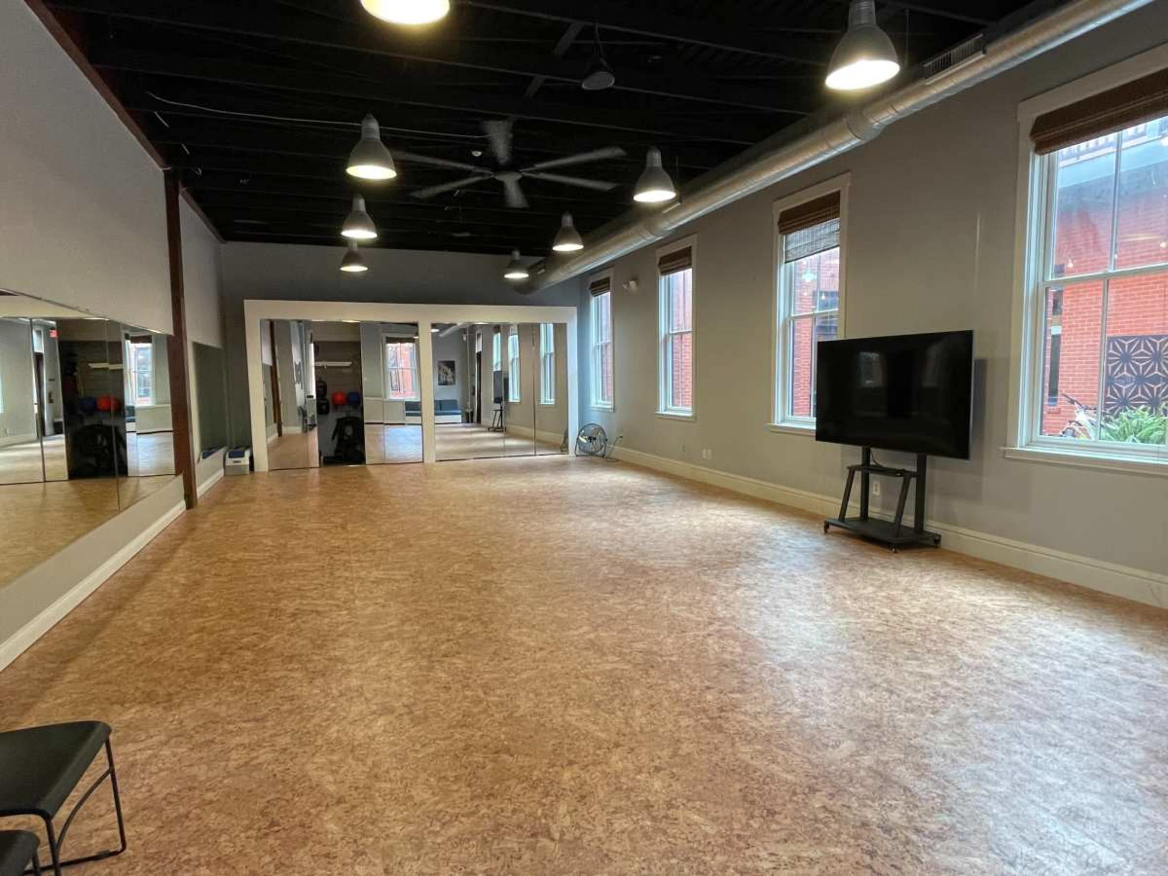 The image shows a spacious, well-lit studio with a smooth floor, large windows, and a television on a stand.