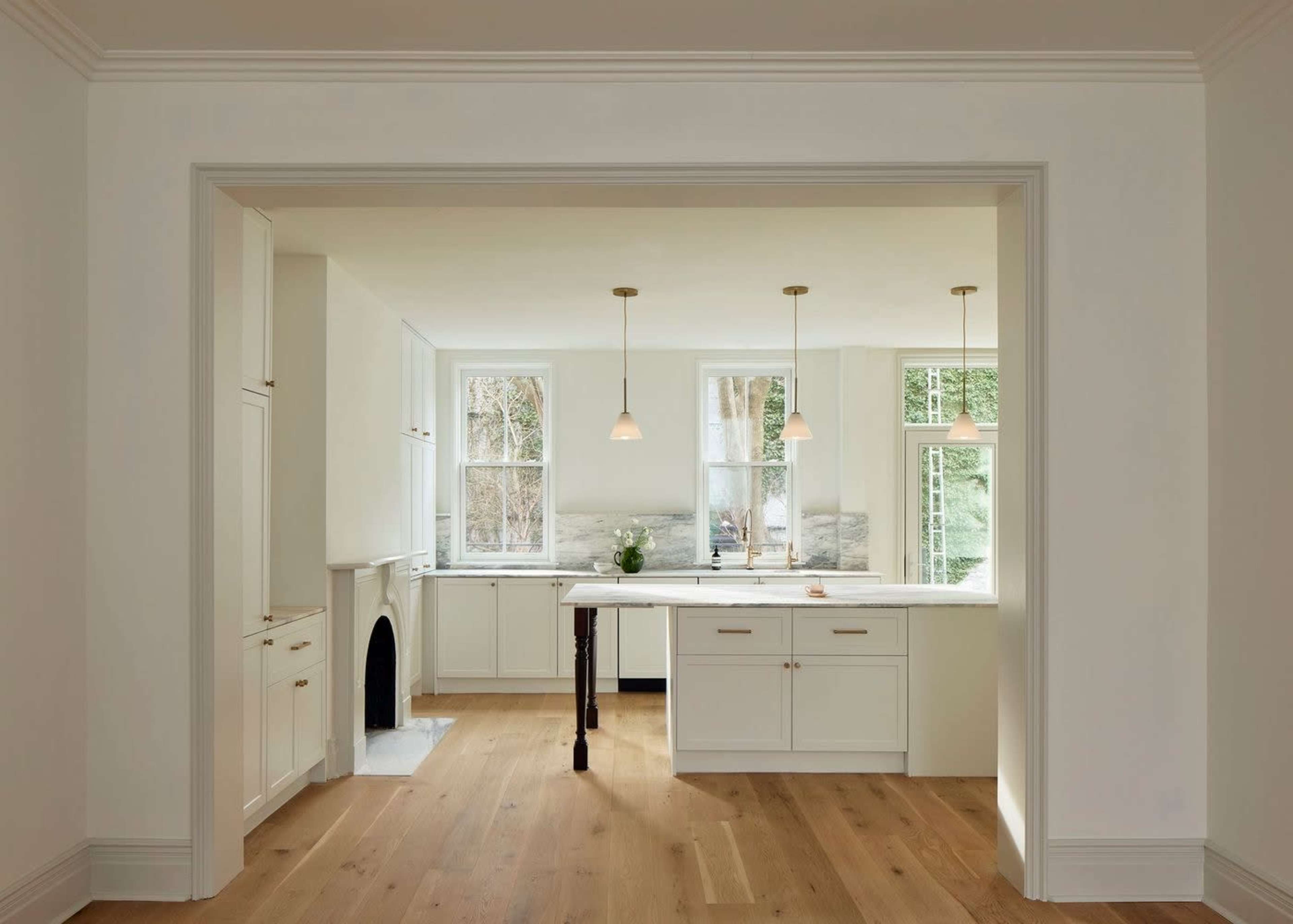 The image shows a modern kitchen with white cabinetry, a large island, and large windows allowing natural light to enter.