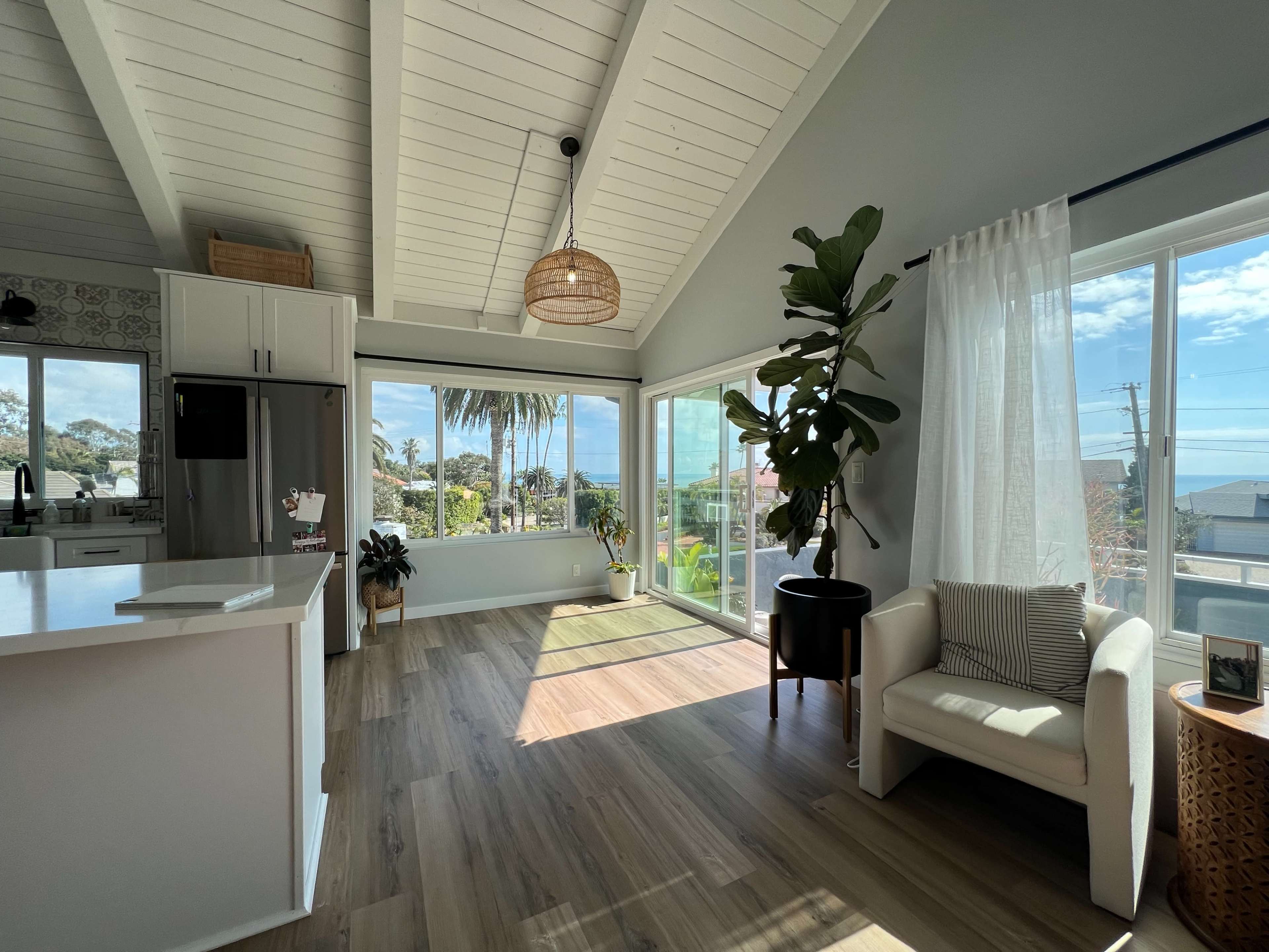 A bright, open living space with a kitchen area, large windows overlooking a garden, and modern furnishings.