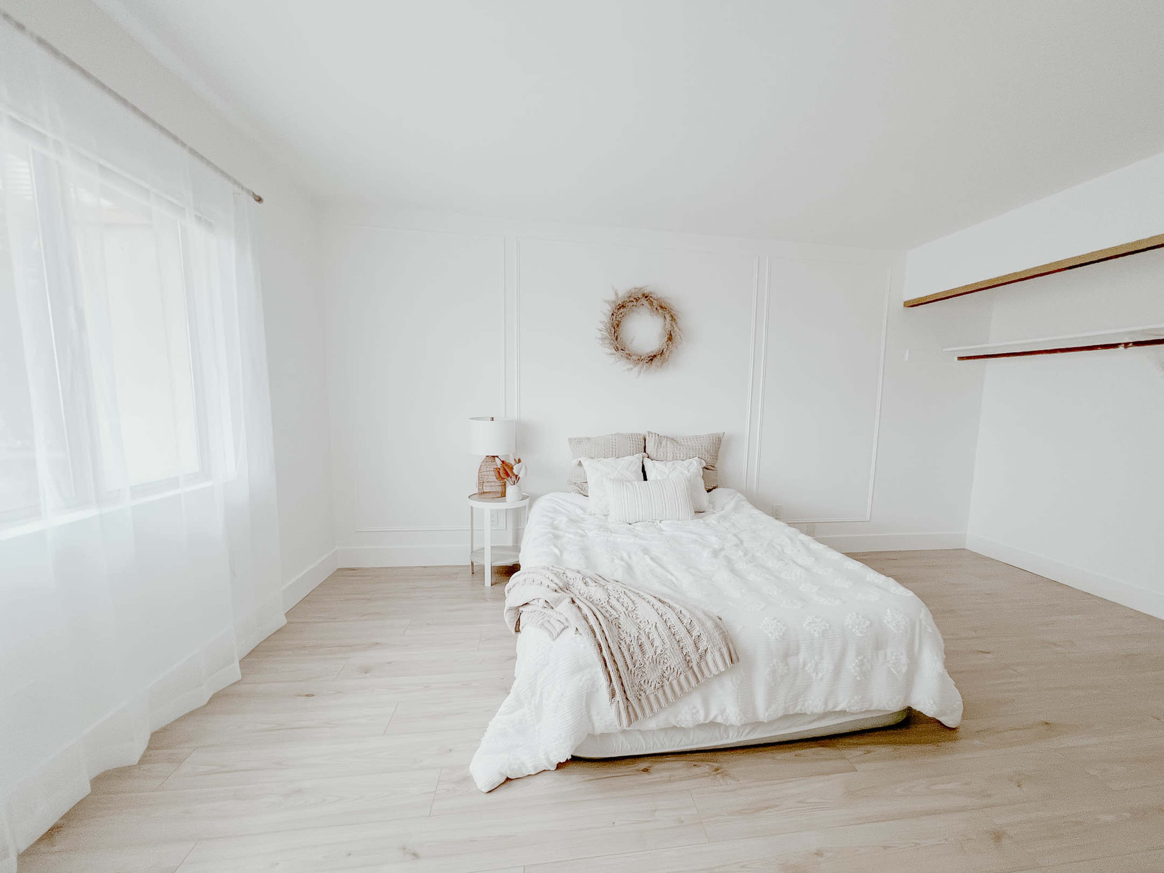 A minimalist bedroom featuring a bed with white bedding, a small bedside table, and a wall-mounted shelf.