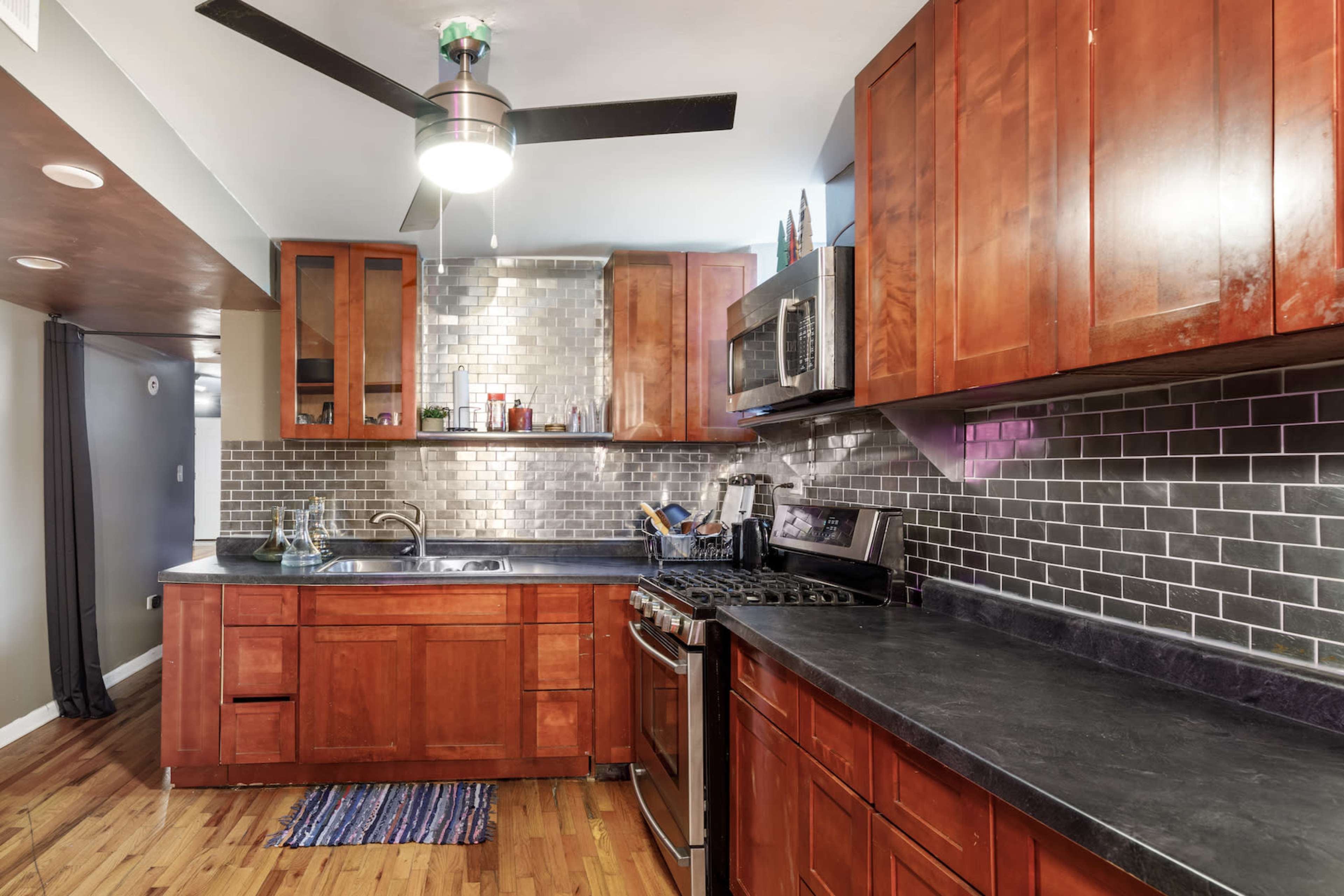 The kitchen features wooden cabinetry, a stainless steel refrigerator and microwave, a gas stove, and a tile backsplash.