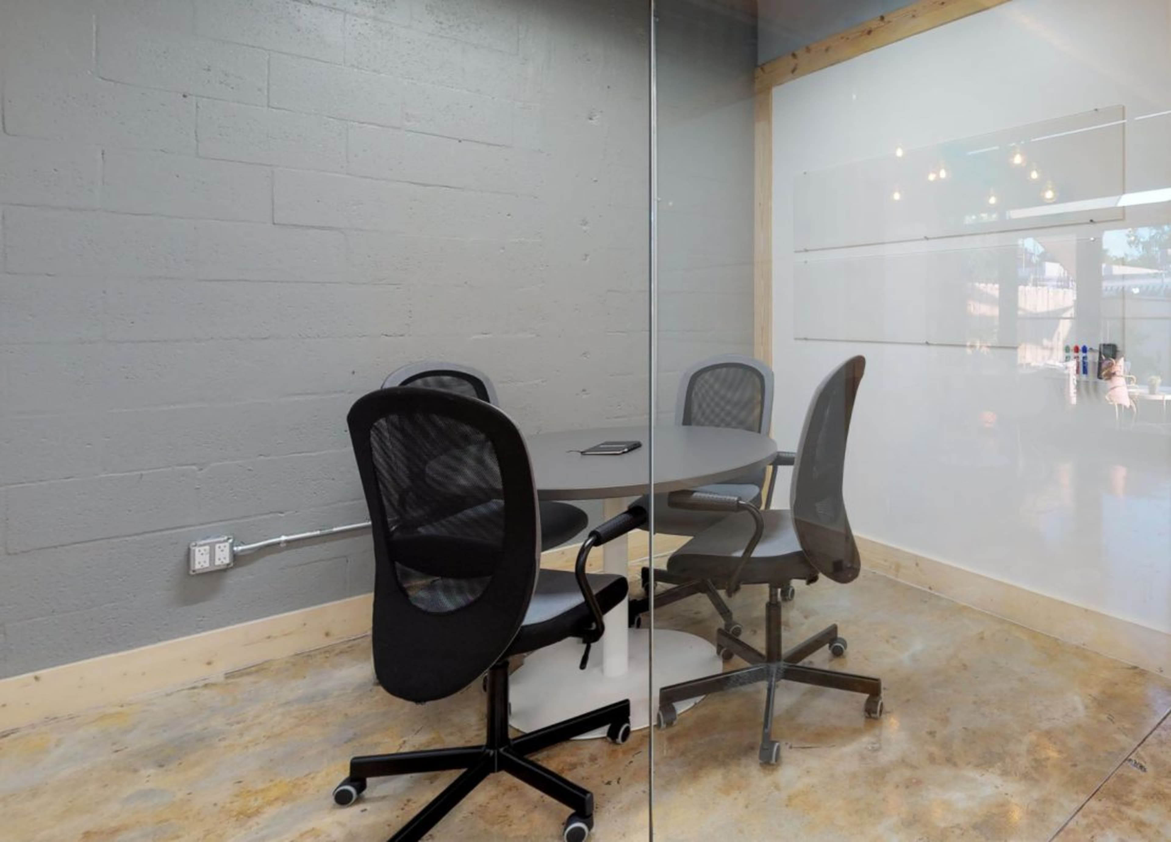 A conference room with a round table and four office chairs, enclosed by glass walls.