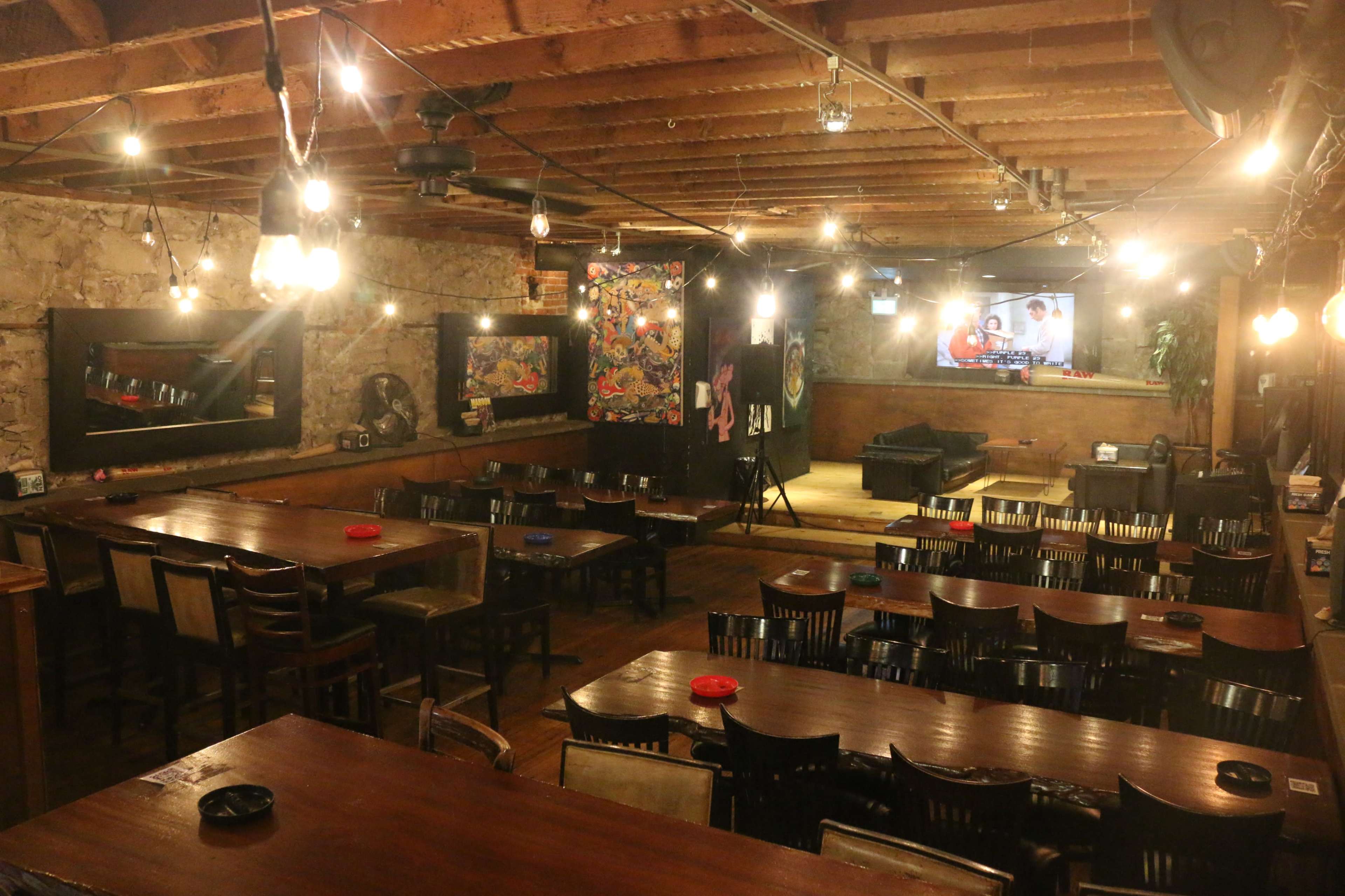 A dimly lit restaurant with wooden tables and chairs, exposed beams, and a large television on one wall.