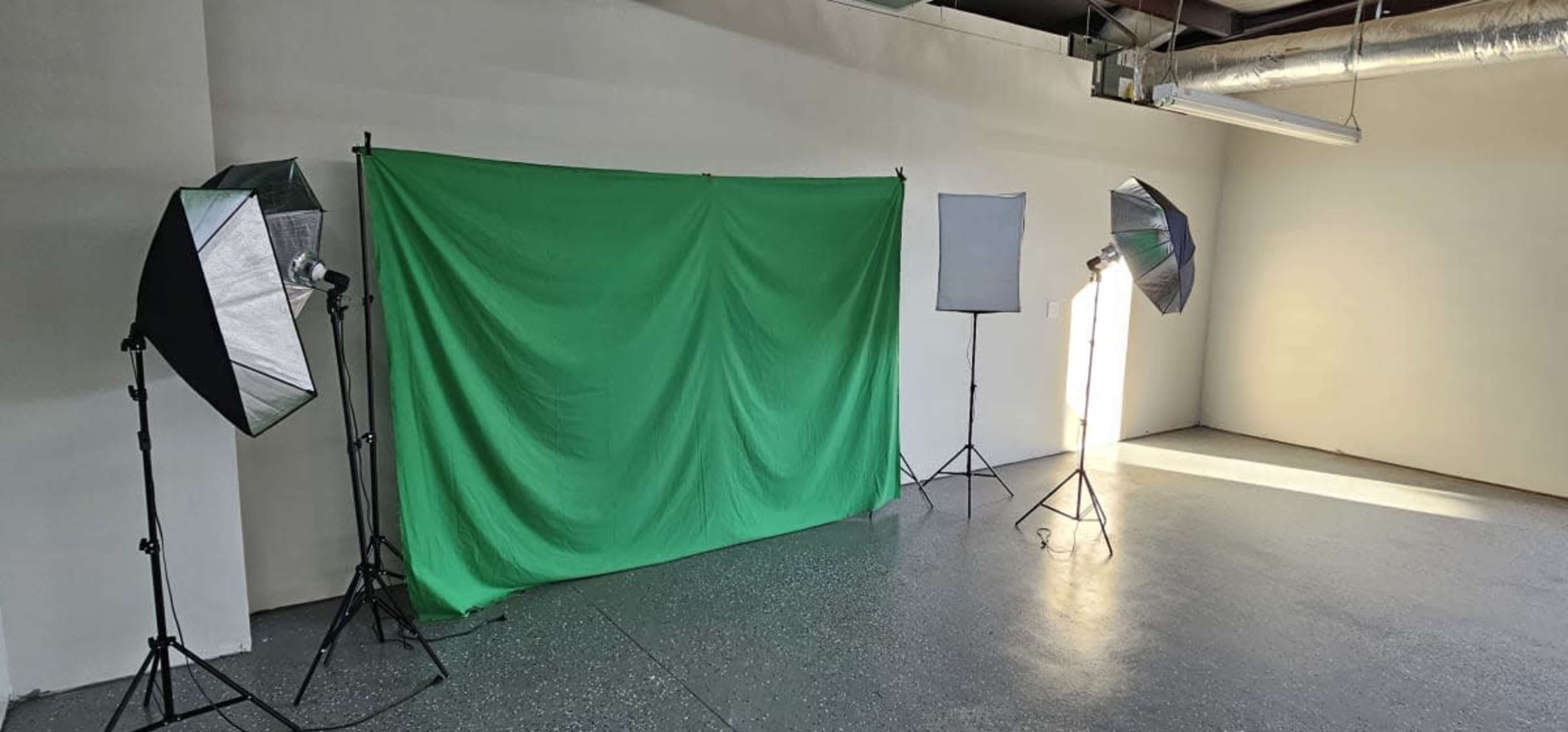 A photography studio with a green backdrop and multiple lighting equipment set up in an empty room.