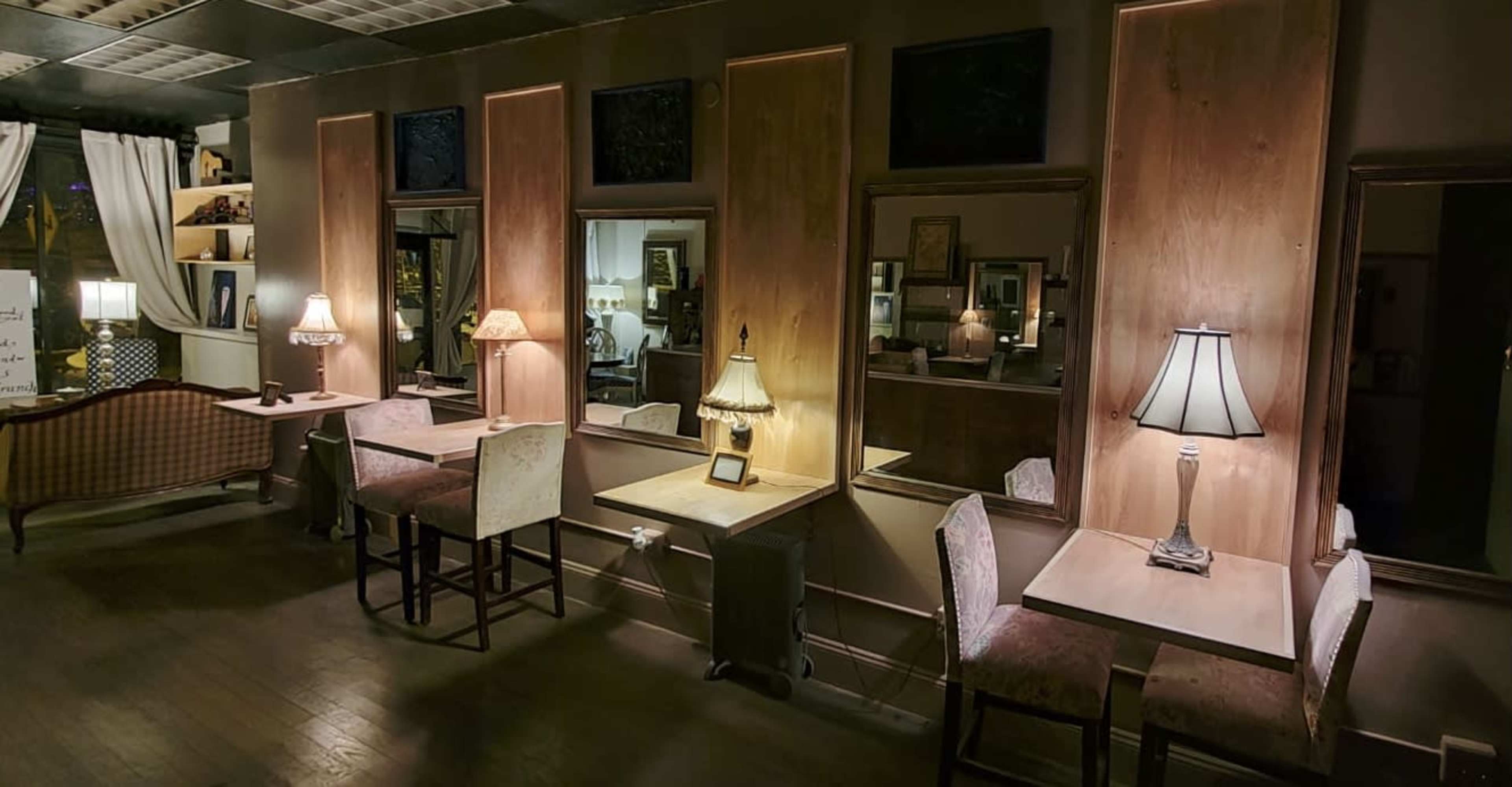 A dimly lit café interior with wooden walls, several small tables, and lamps providing soft illumination.