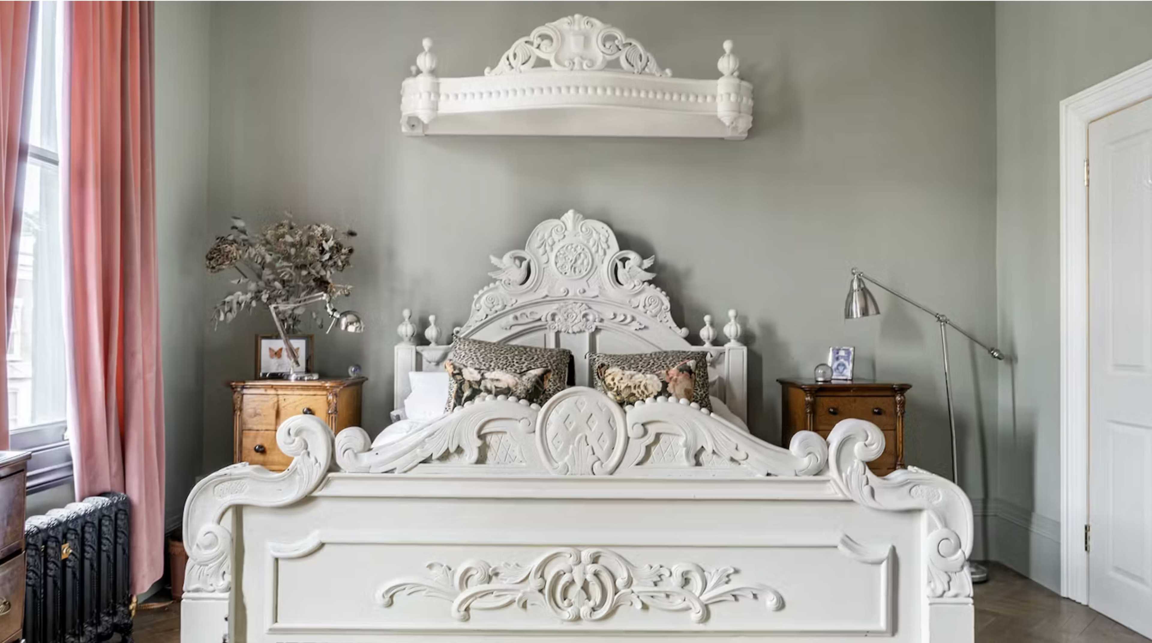 A spacious bedroom featuring a large white ornate bed, two bedside tables, and a decorative wall mounted shelf above the bed.
