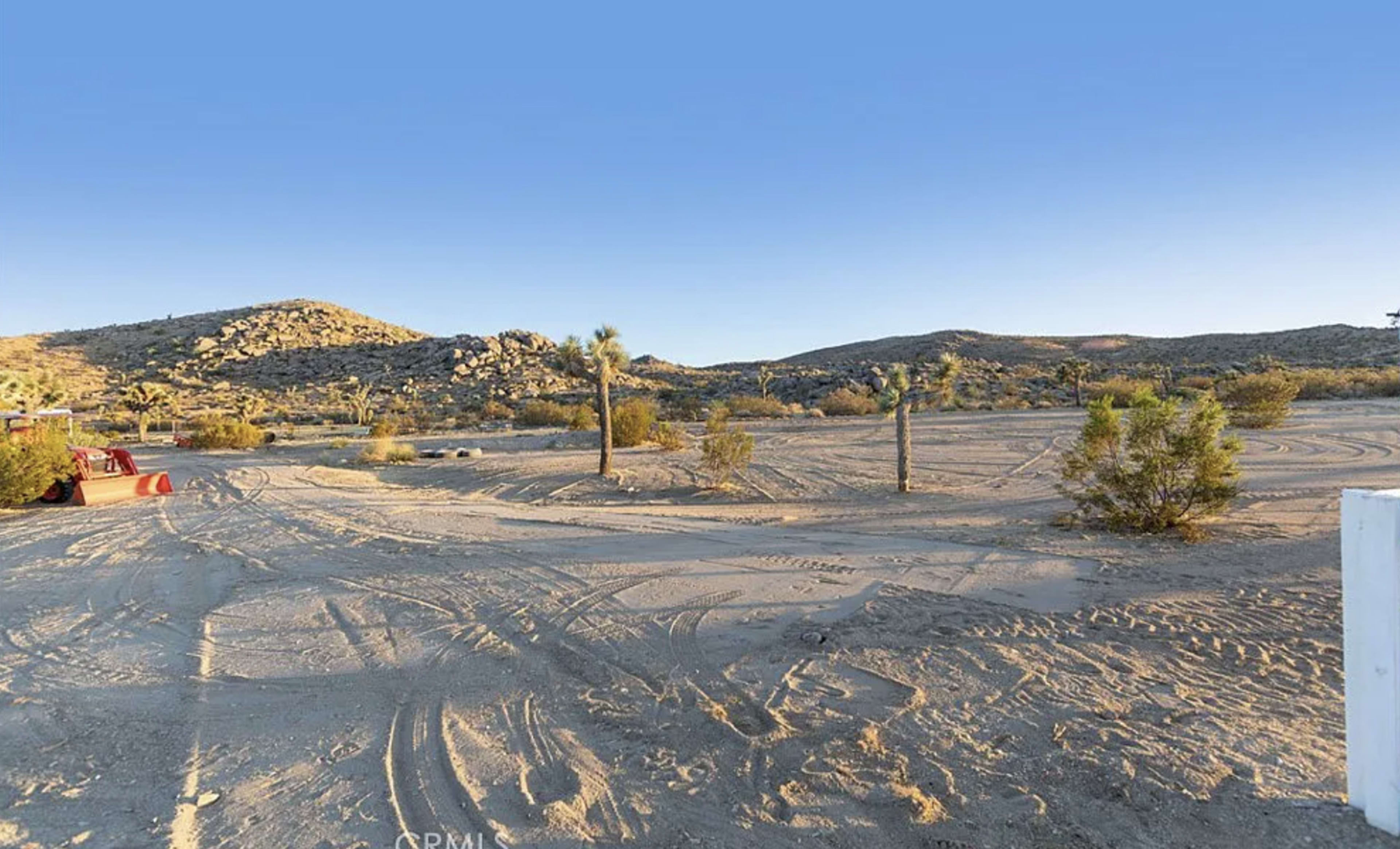 The image shows a sandy desert landscape with sparse vegetation and hills in the background.