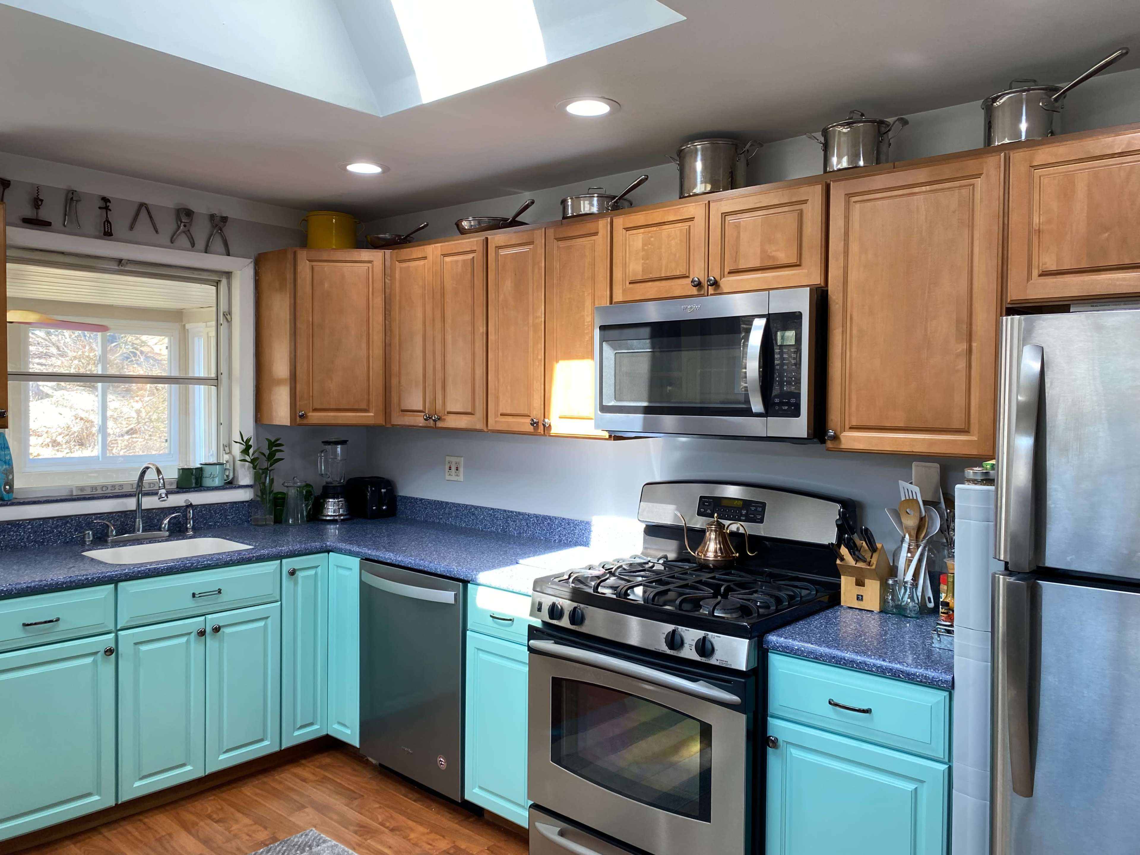 The kitchen features wooden cabinets, a blue countertop, and stainless steel appliances, with a skylight allowing natural light to enter.