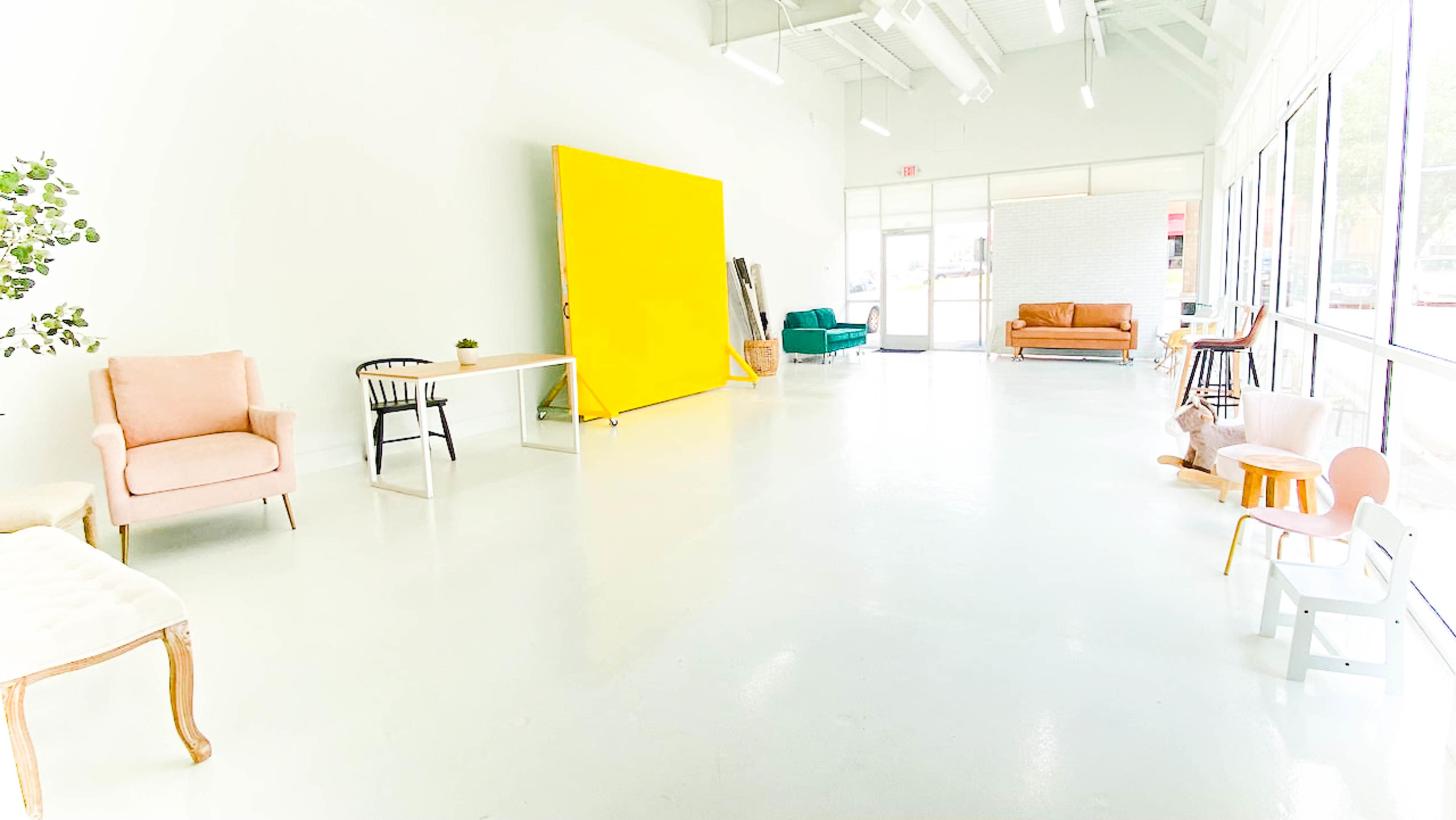 A spacious room with a bright yellow backdrop, various seating options including chairs and a couch, and large windows allowing natural light to fill the space.