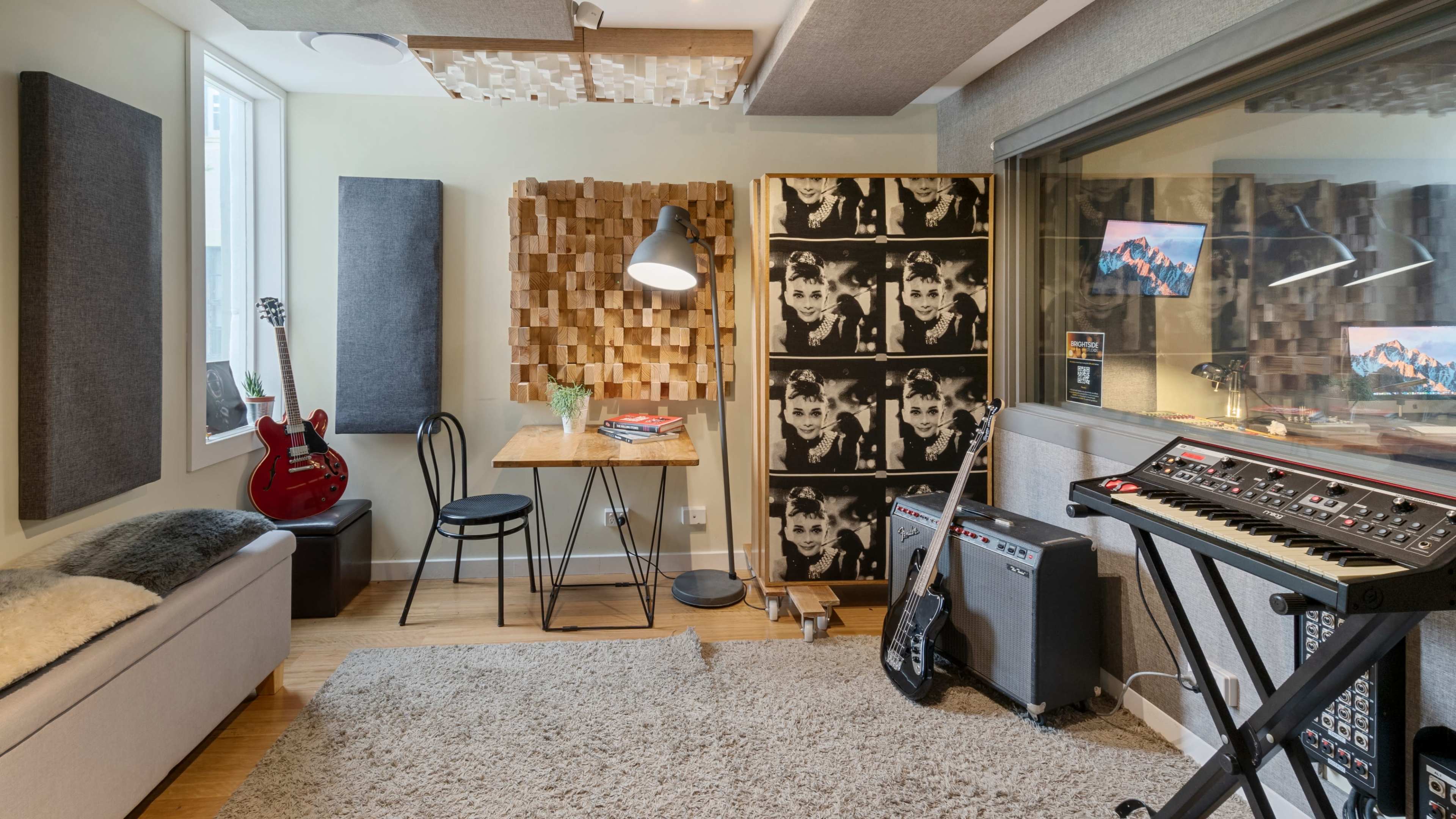 The image features a cozy sound studio with a guitar, keyboard, and acoustic panels, along with a small table and chairs.