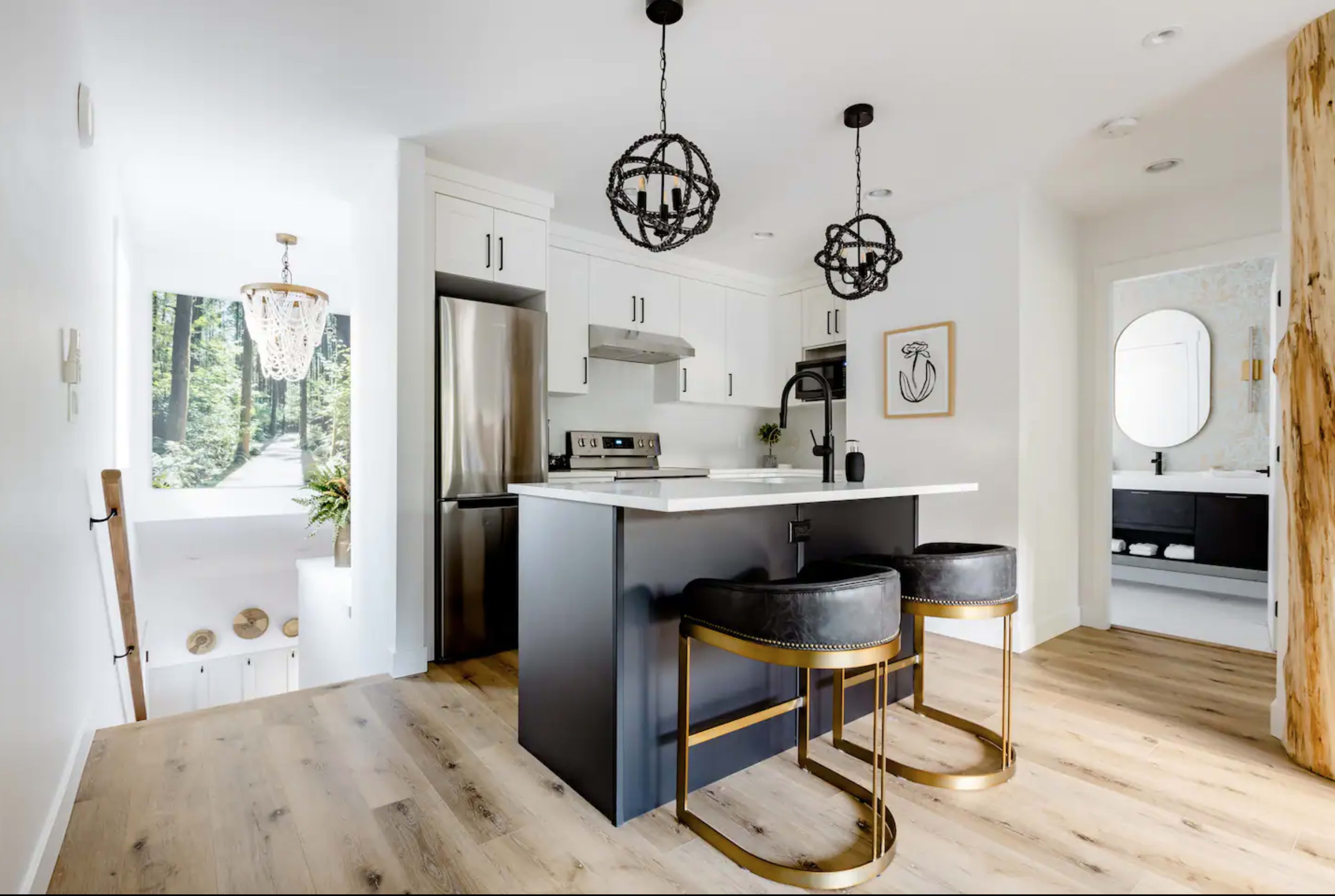 A modern kitchen with a central island, two black bar stools, and pendant lighting.