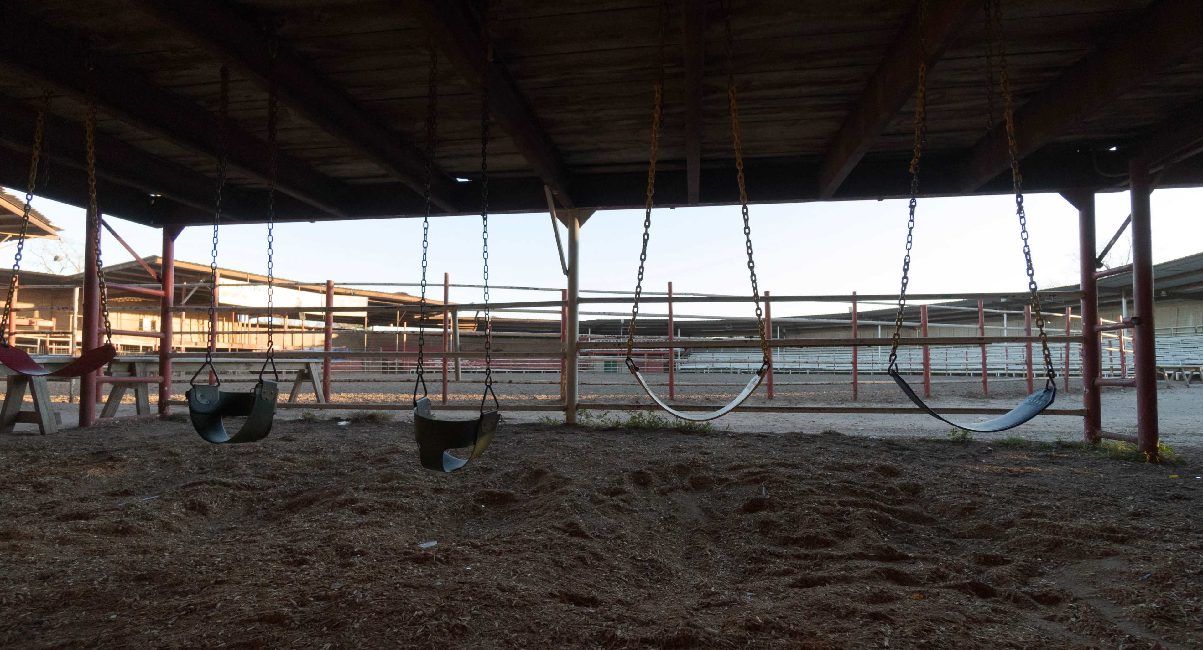 A row of swings hangs beneath a wooden structure in an empty playground area.