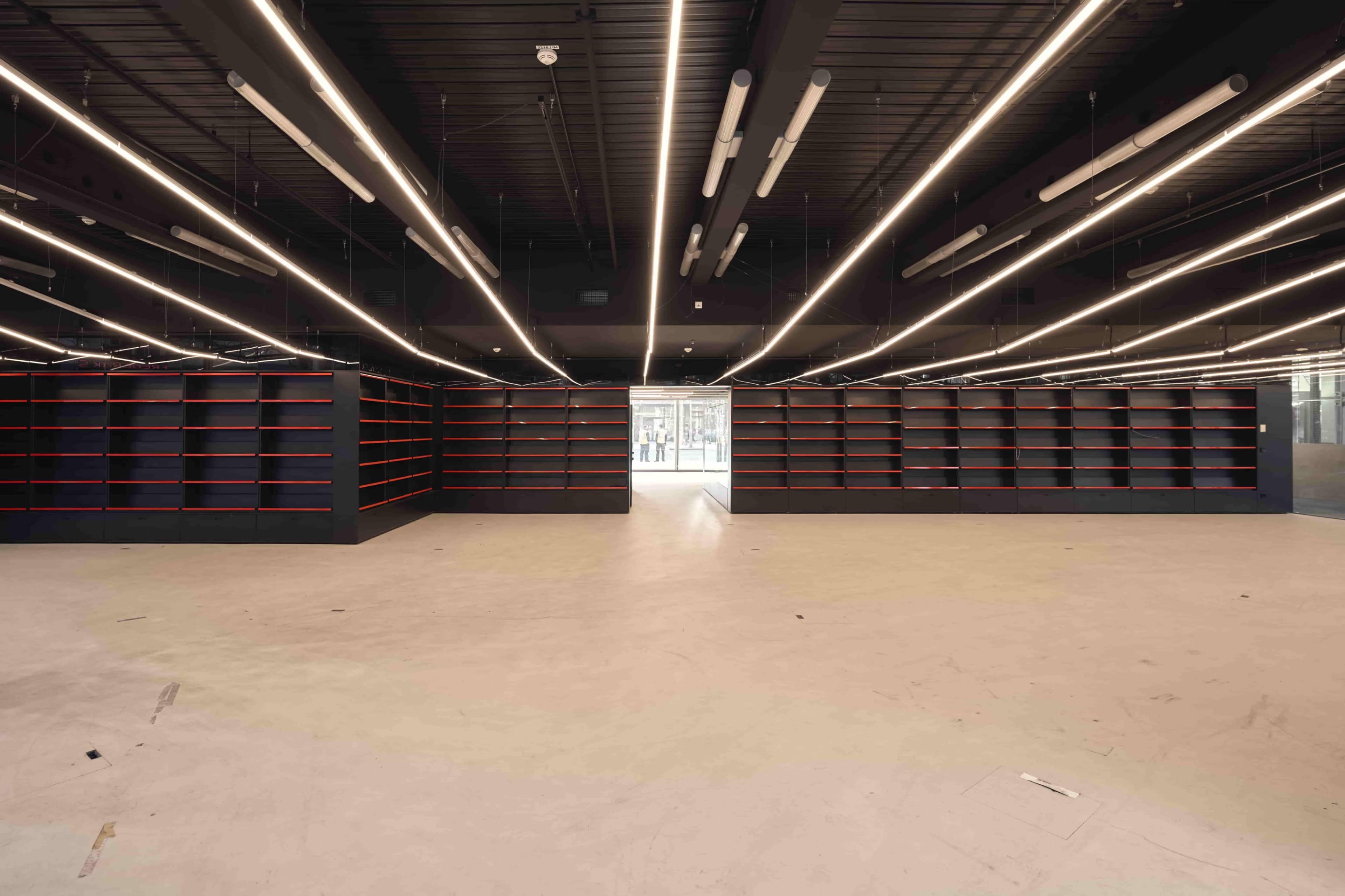 The image shows an empty retail space with black shelving units and overhead lighting, devoid of merchandise.