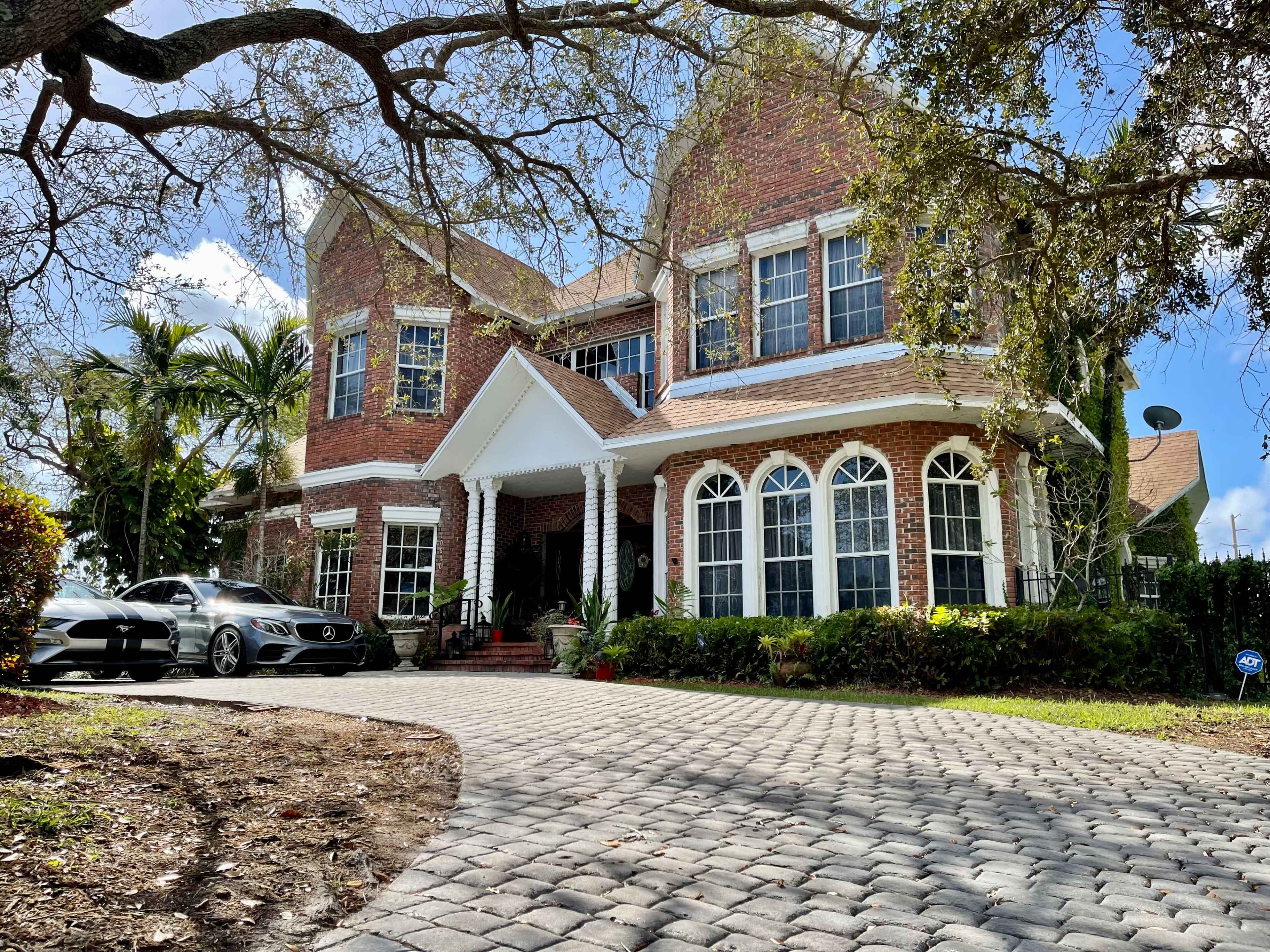 A two-story brick house with a prominent entryway and two vehicles parked in the driveway.