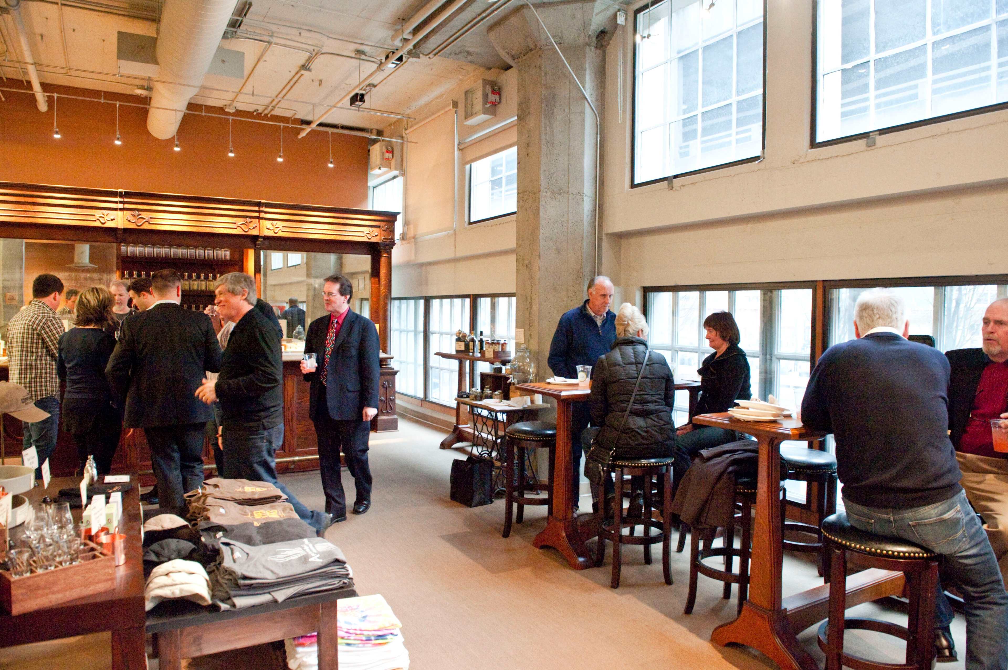A vibrant gathering takes place in a well-lit lounge with people conversing at high-top tables and a bar in the background.