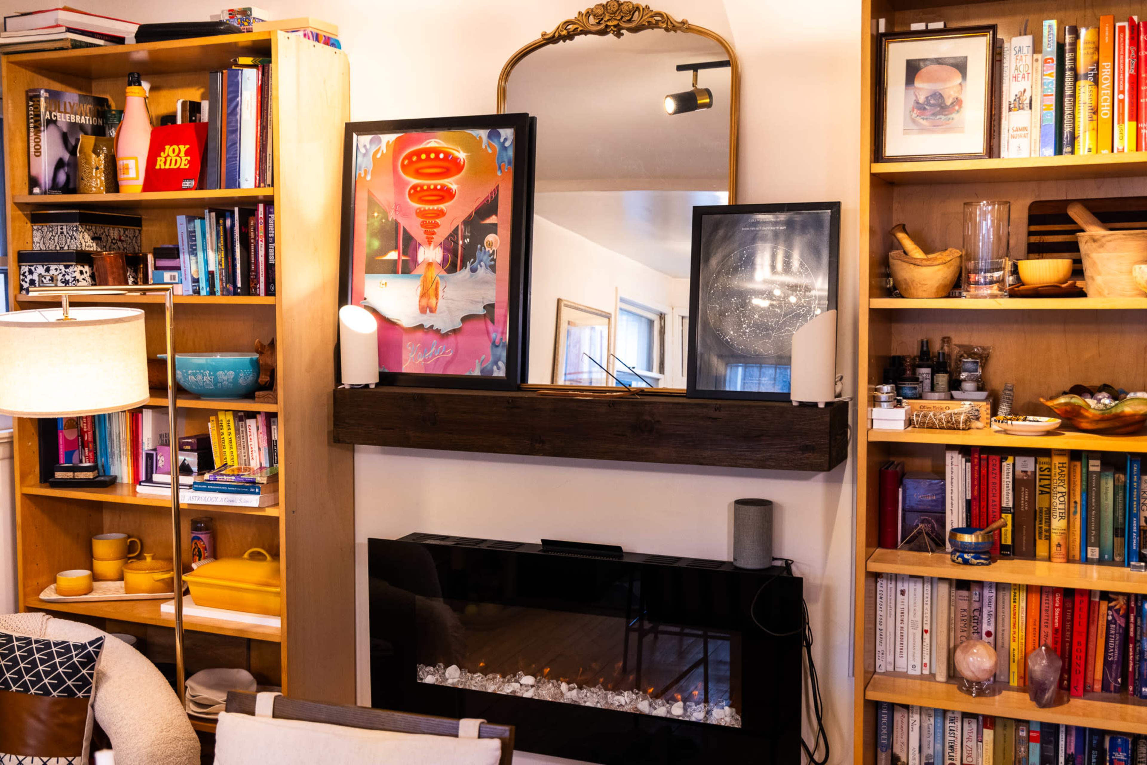 The image shows a cozy living room with a wooden shelf above a modern electric fireplace, flanked by bookshelves filled with various books and decorative items.