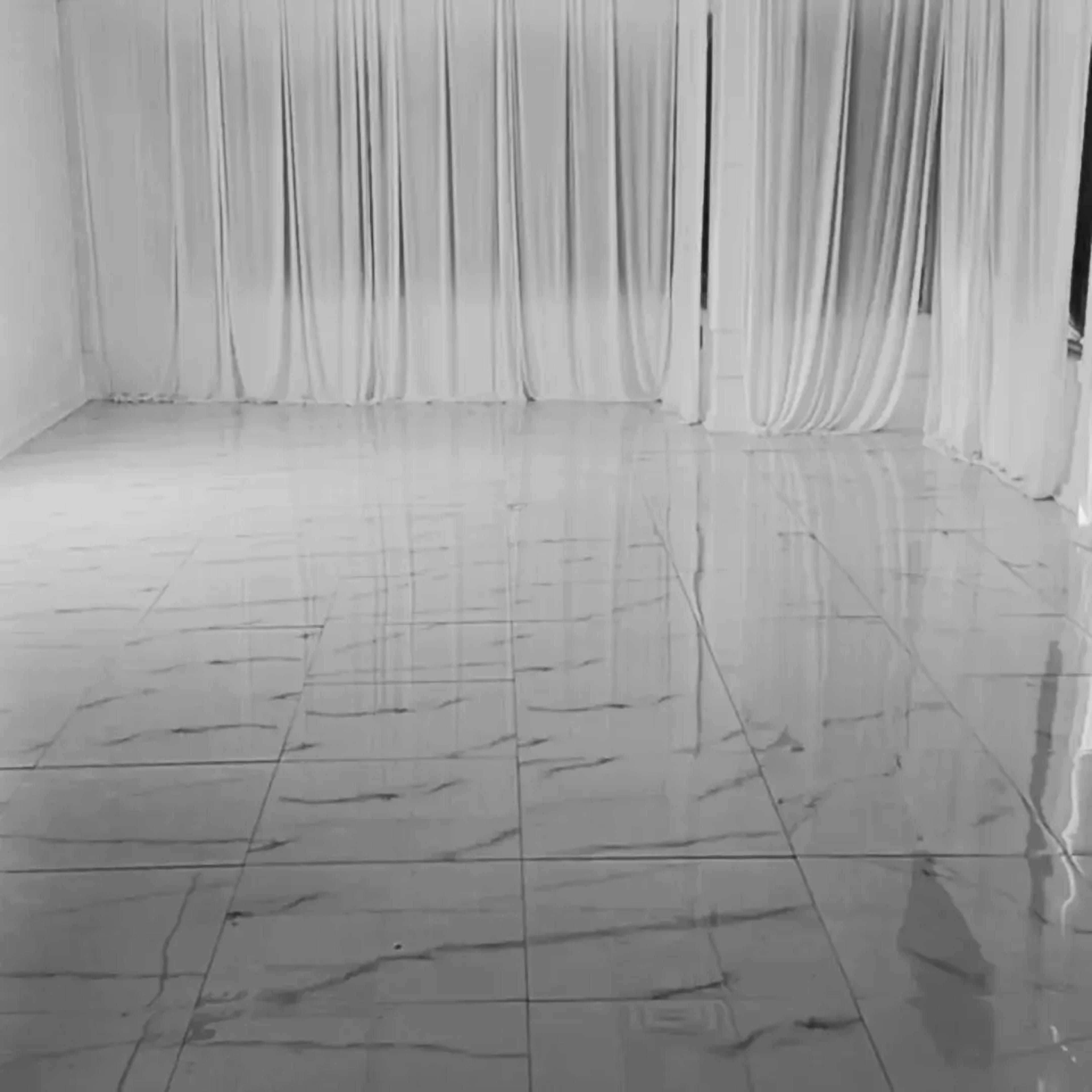 A spacious room with glossy marble tiles and white curtains draping from the ceiling.