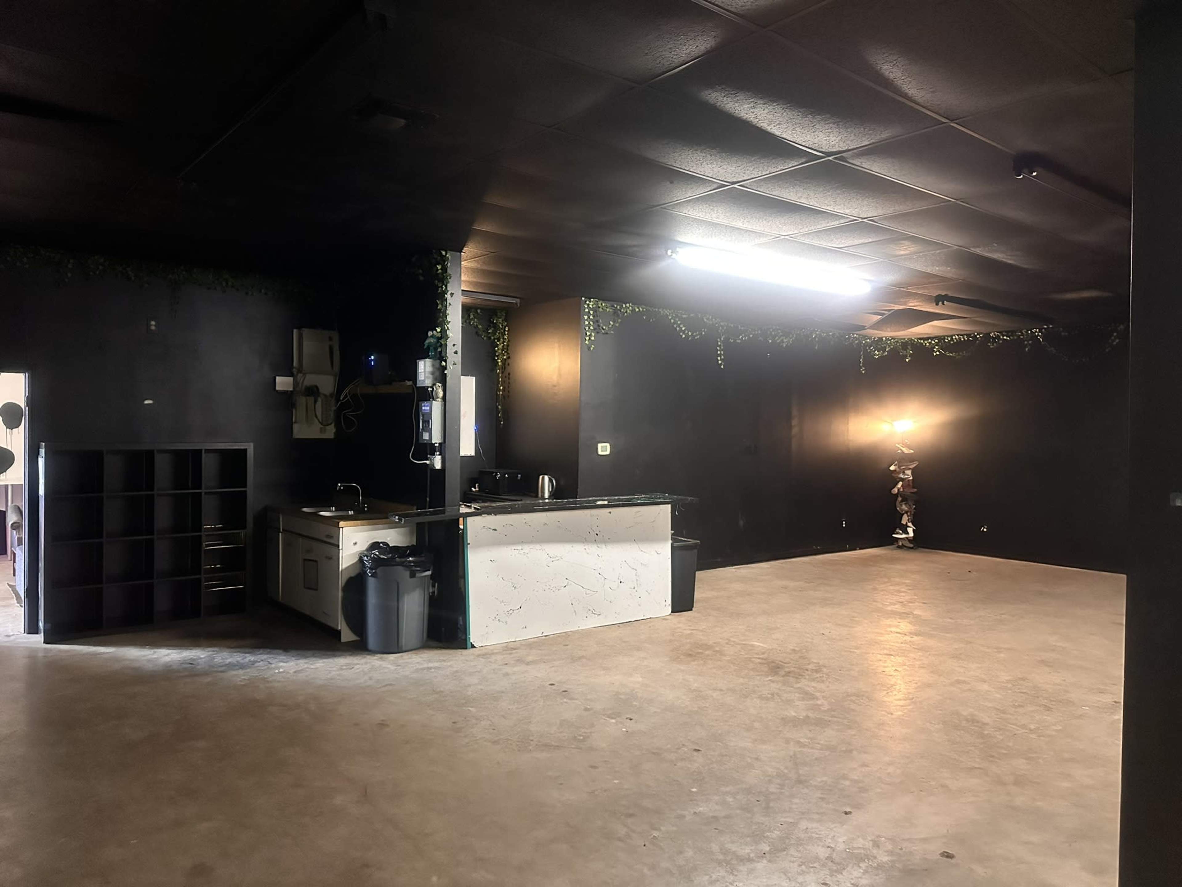 The image shows an empty room with dark walls, a bar area, and a lamp in the corner.