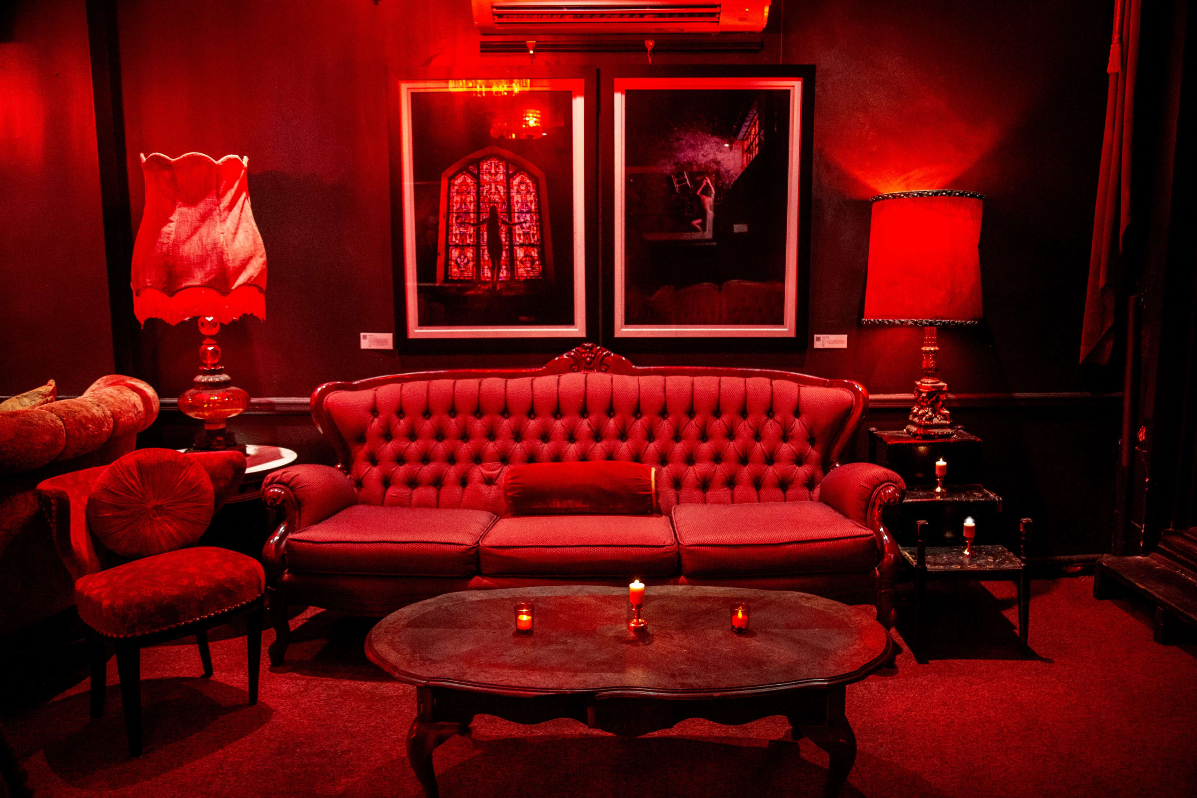 The room features a red-themed seating area with a tufted sofa, a round coffee table, and two lamps, accompanied by framed artwork on the walls.