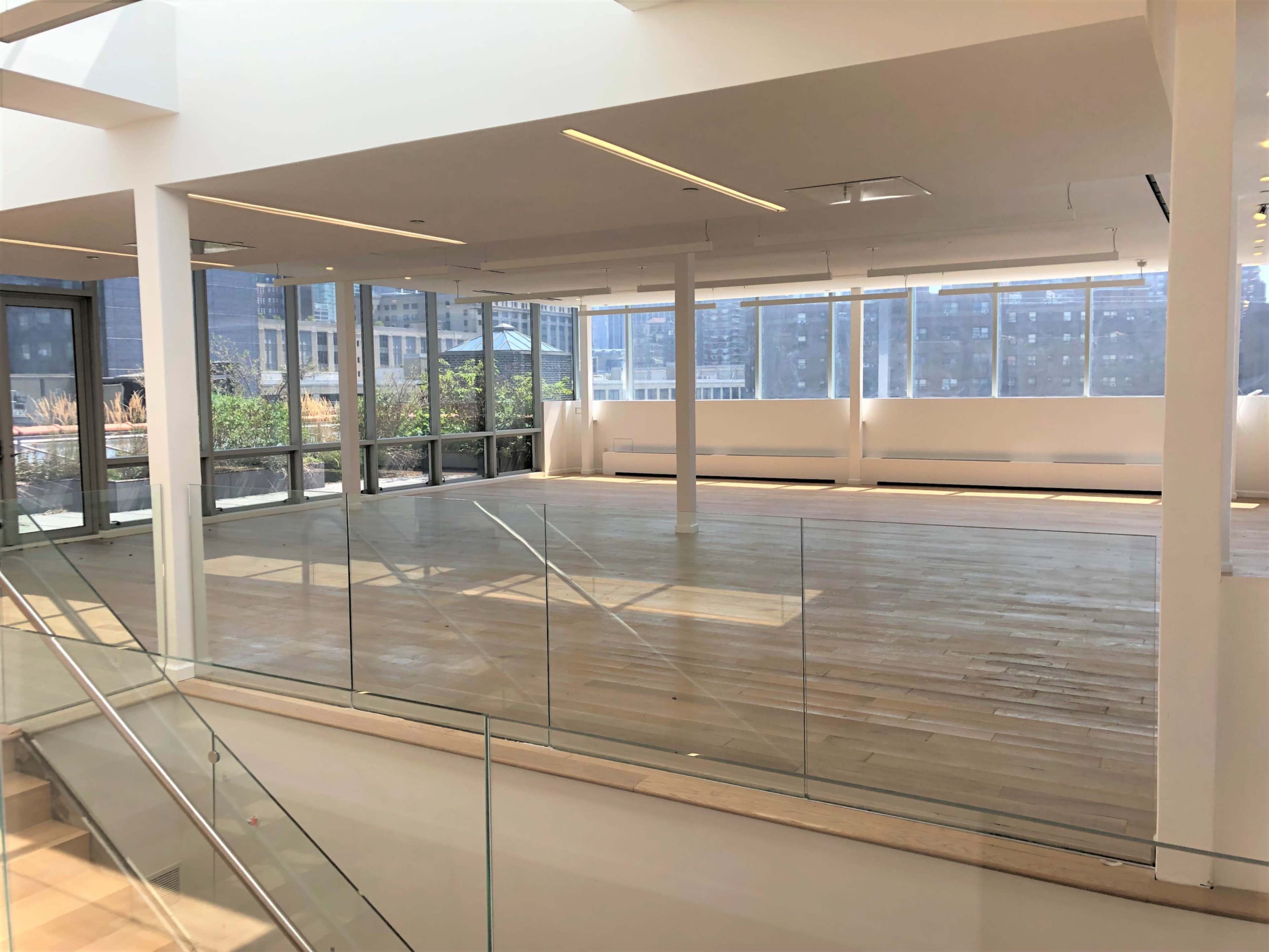 A spacious, sunlit interior features wooden flooring and large windows overlooking a cityscape.