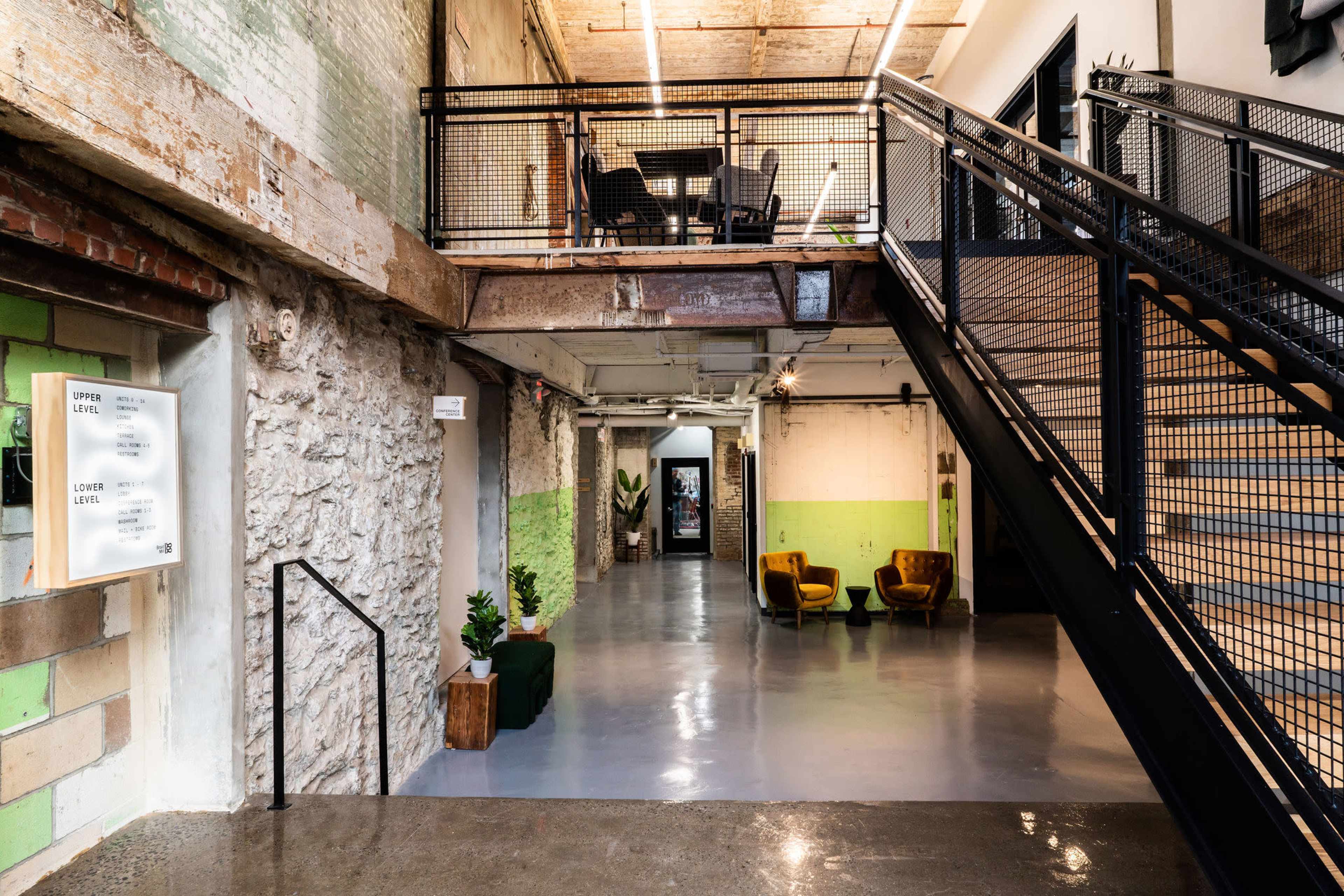 A spacious interior corridor featuring a staircase, a seating area with yellow chairs, and walls with a green and gray color scheme.