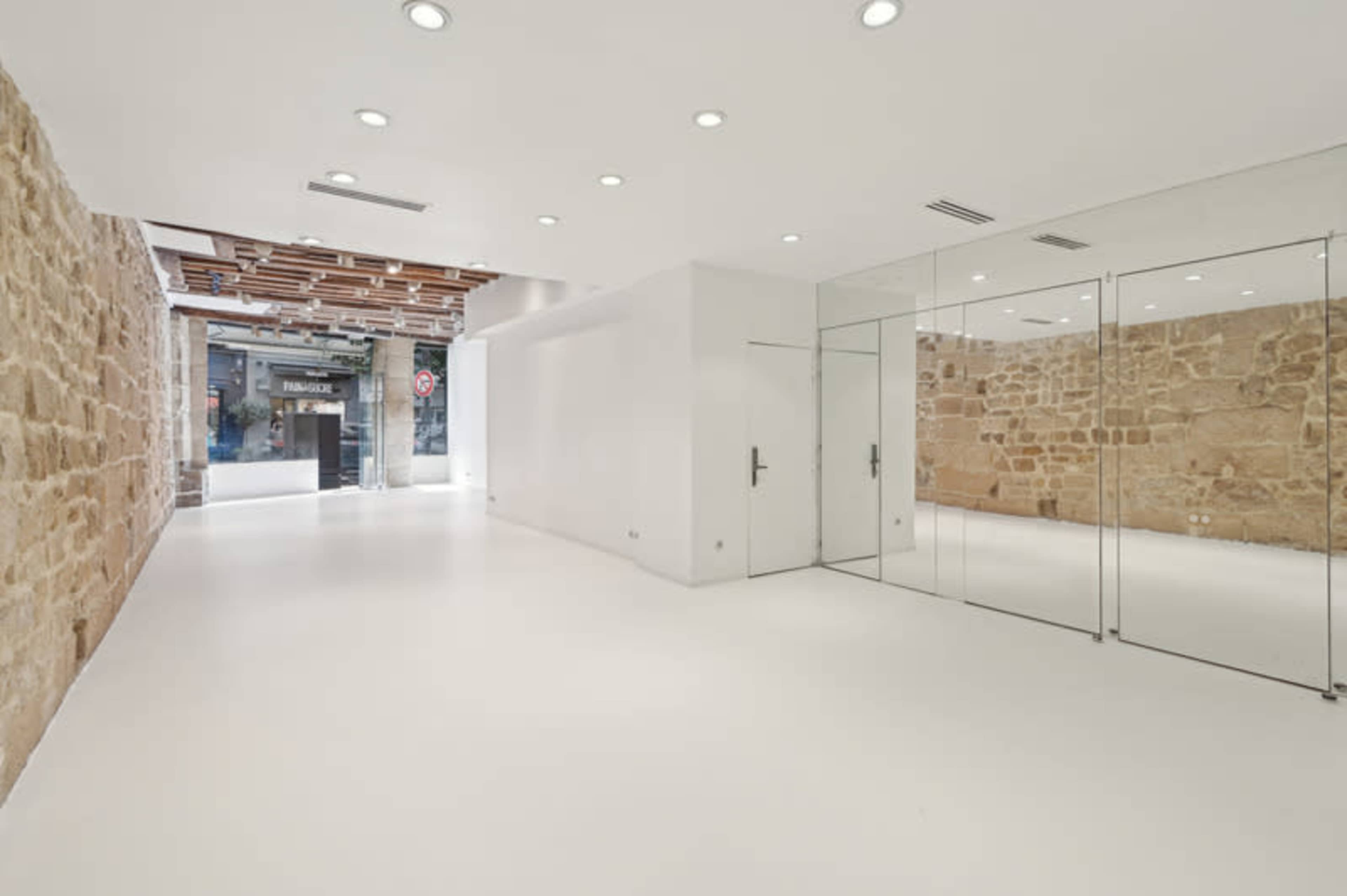 The image shows a spacious, modern interior with a white floor and glass walls, featuring a blend of smooth white surfaces and exposed stone.