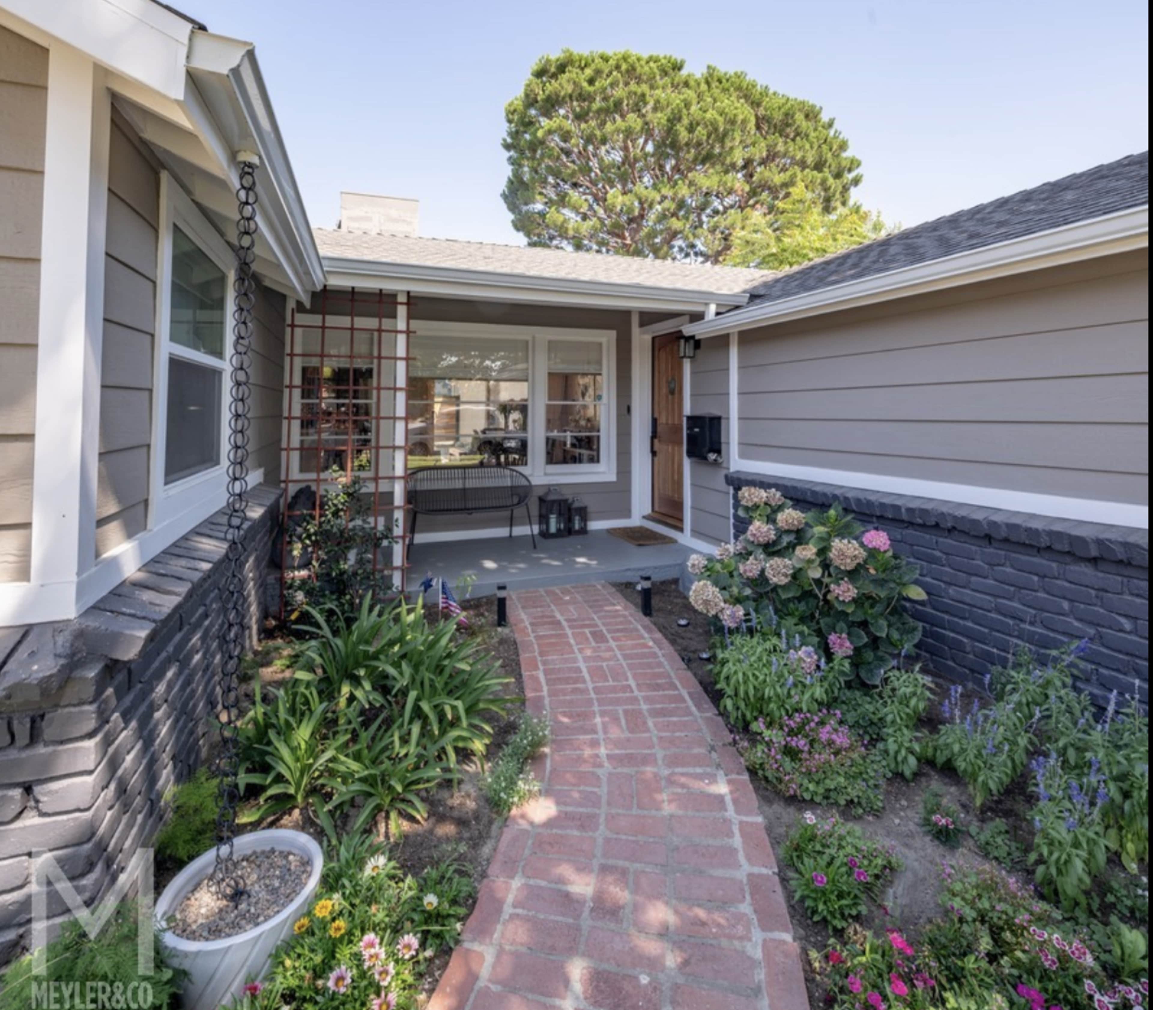 A brick pathway leading through a landscaped front yard toward the entrance of a house.
