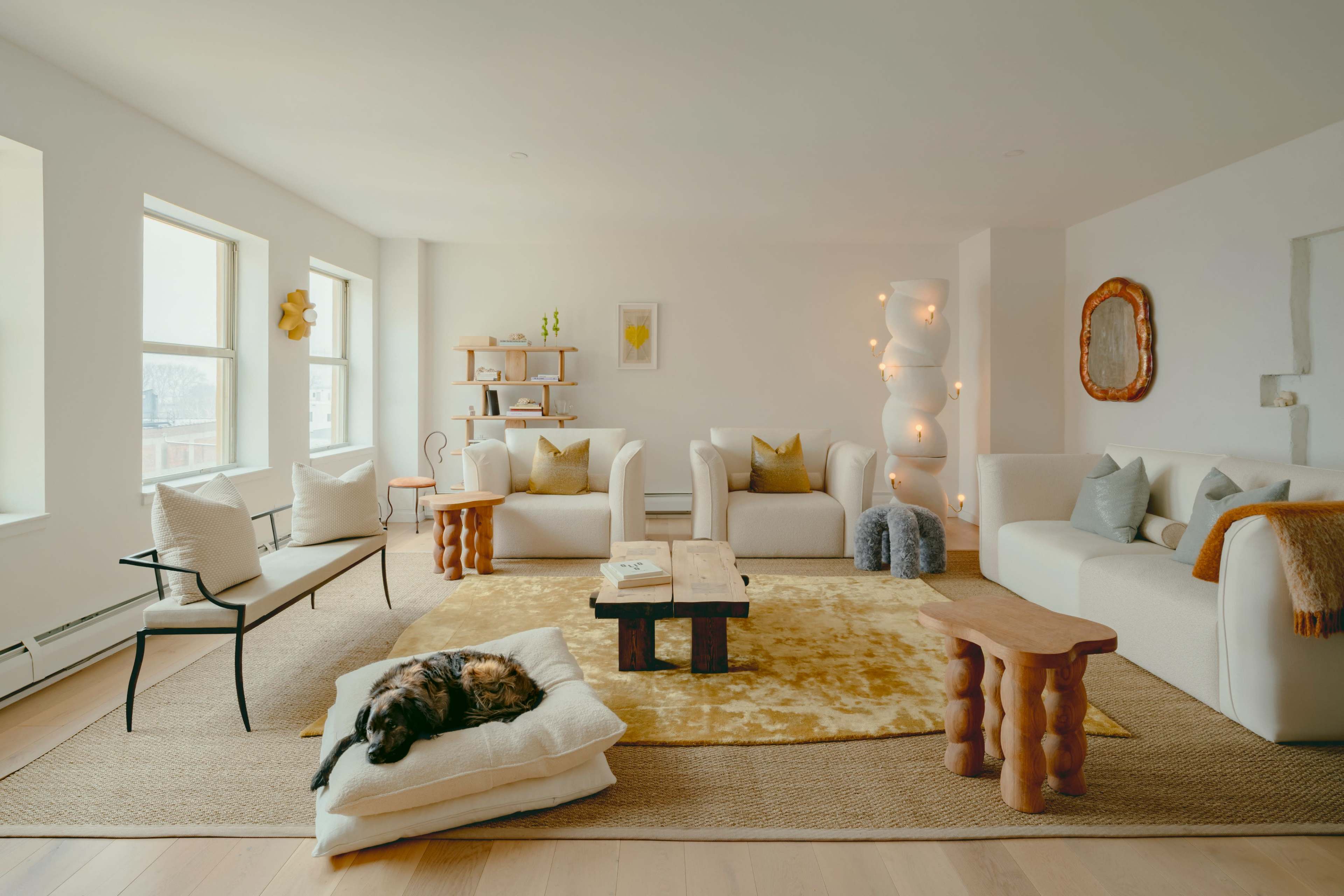 The living room features light-colored furniture, a large area rug, wooden tables, and a sleeping dog on a cushion.